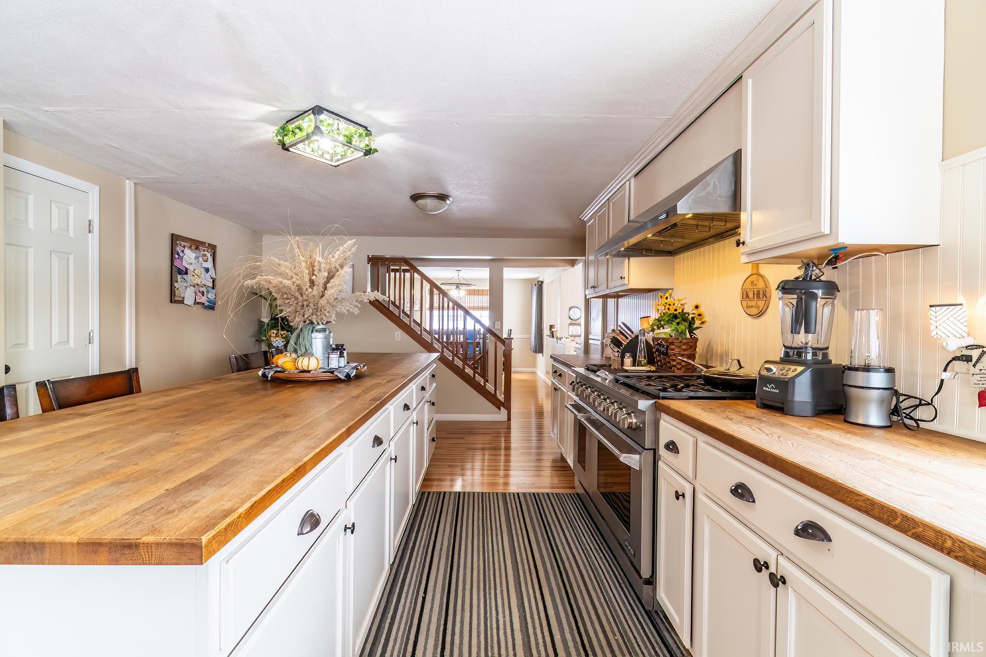 Kitchen with wooden counters, double oven range, range hood, white cabinets, and dark wood-style flooring
