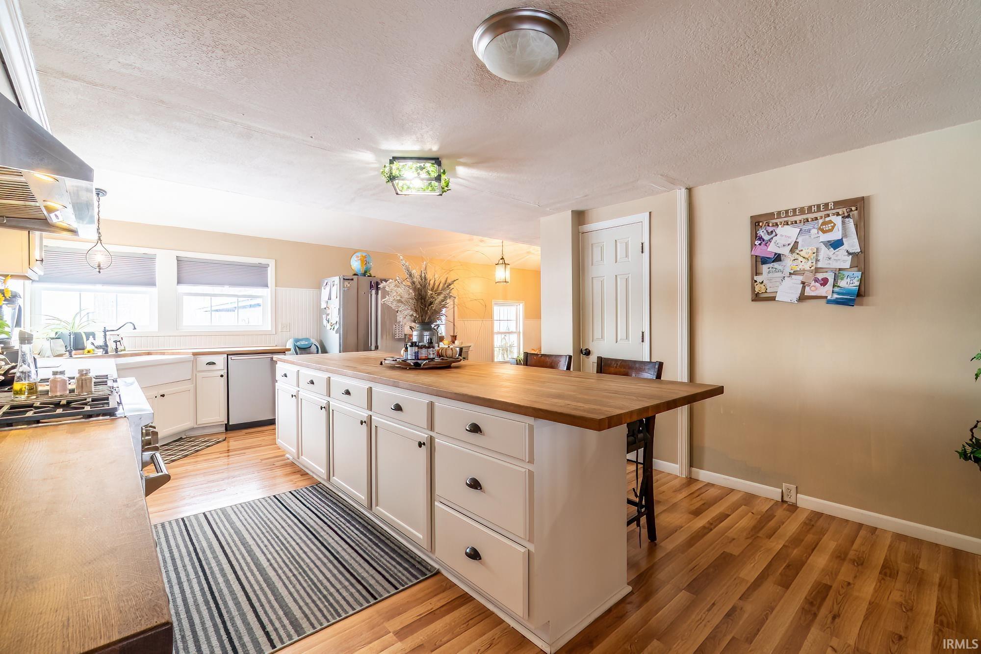 Kitchen with wood counters, healthy amount of natural light, white cabinets, a breakfast bar, and a textured ceiling