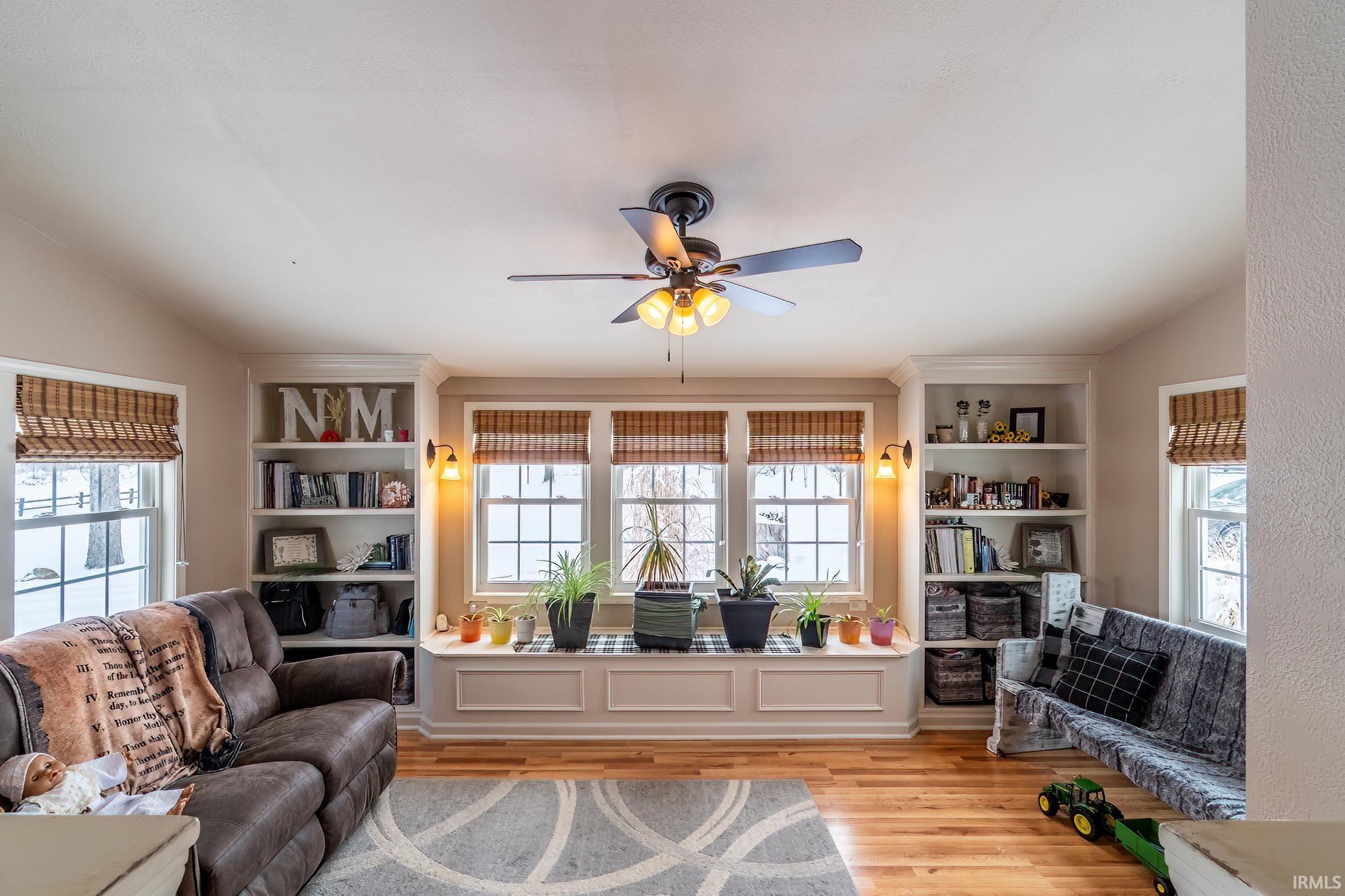 Sitting room with built in shelves, lofted ceiling, healthy amount of natural light, light wood-style floors, and a ceiling fan