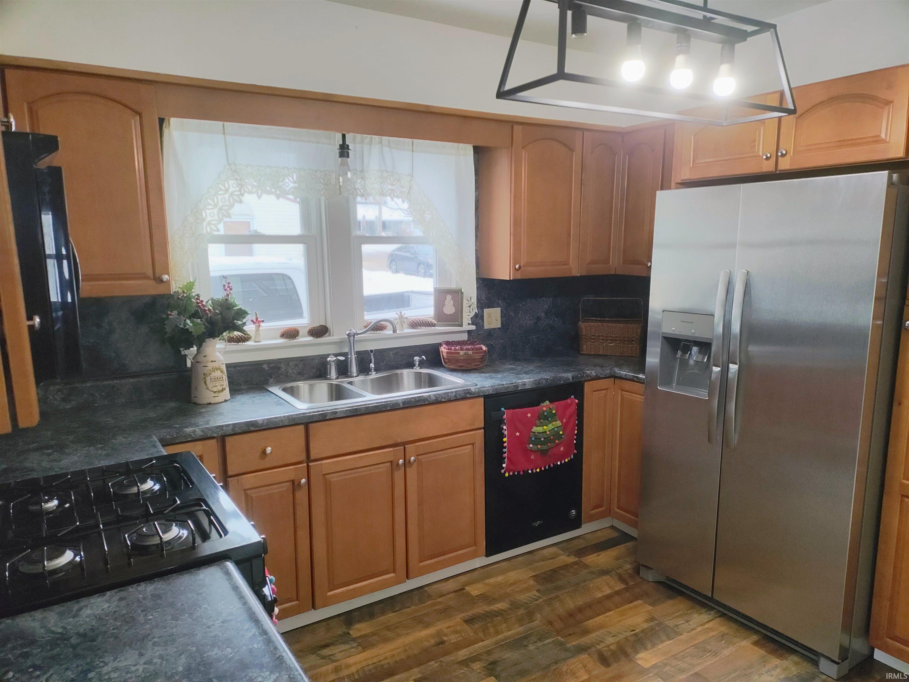 Kitchen featuring black appliances, dark countertops, dark wood-style floors, and brown cabinetry