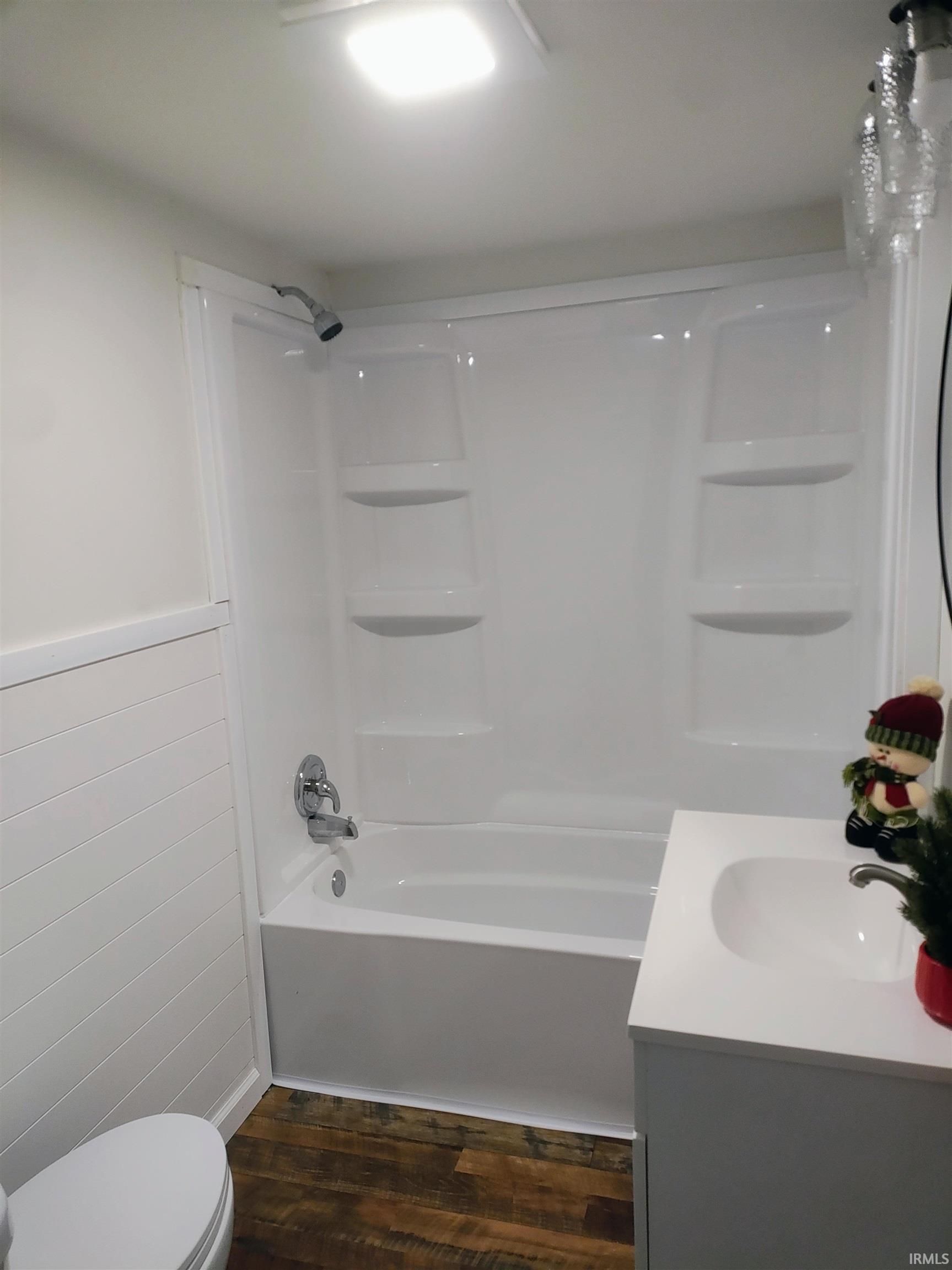 Bathroom with vanity, bathing tub / shower combination, wainscoting, tile walls, and dark wood-type flooring