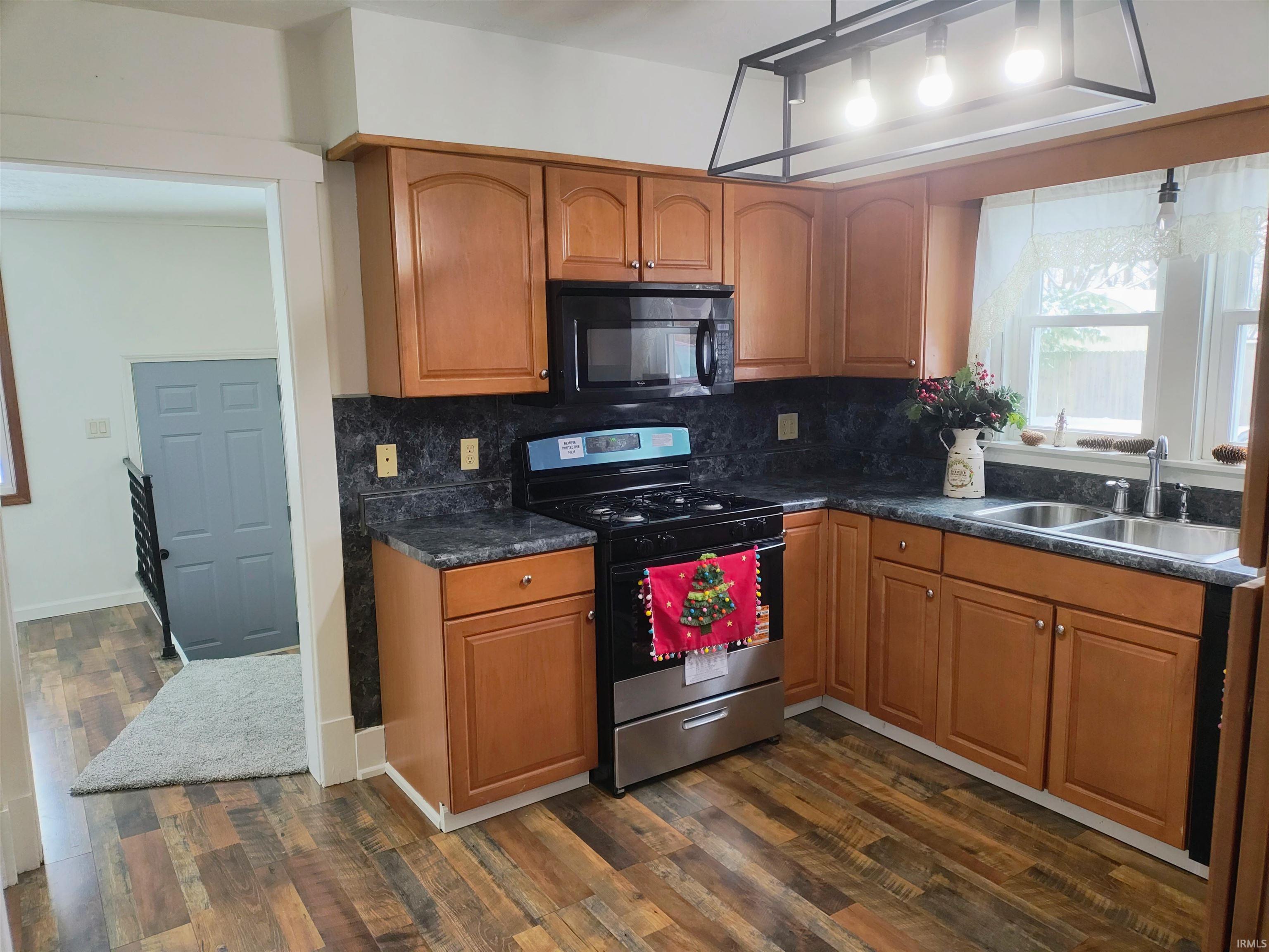 Kitchen featuring stainless steel gas range oven, black microwave, brown cabinetry, and dark countertops