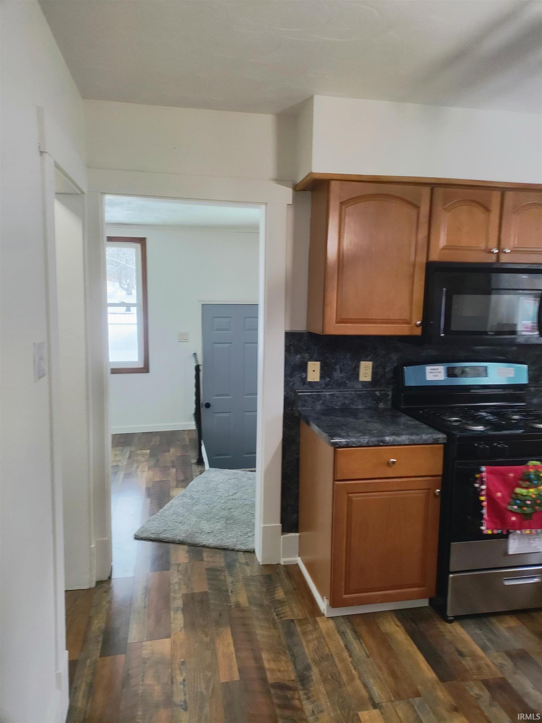 Kitchen with stainless steel range oven, brown cabinets, black microwave, and dark wood finished floors