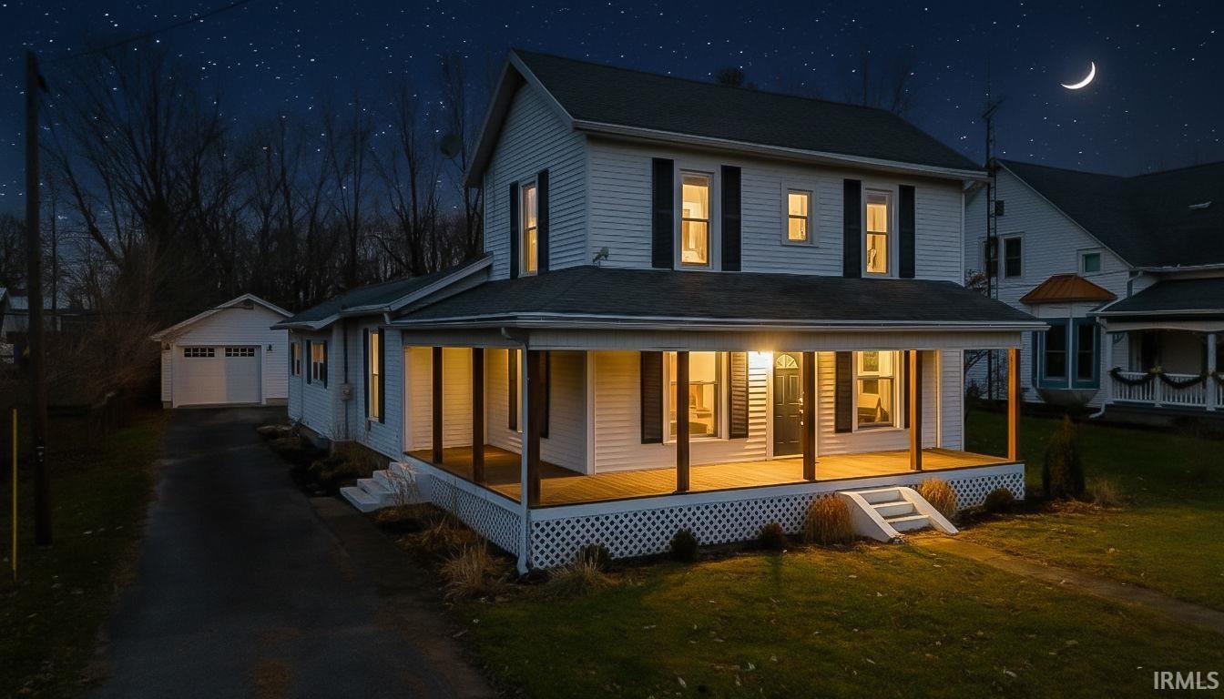Back of house at twilight with a large porch, an outdoor structure, a detached garage, asphalt driveway, and a yard