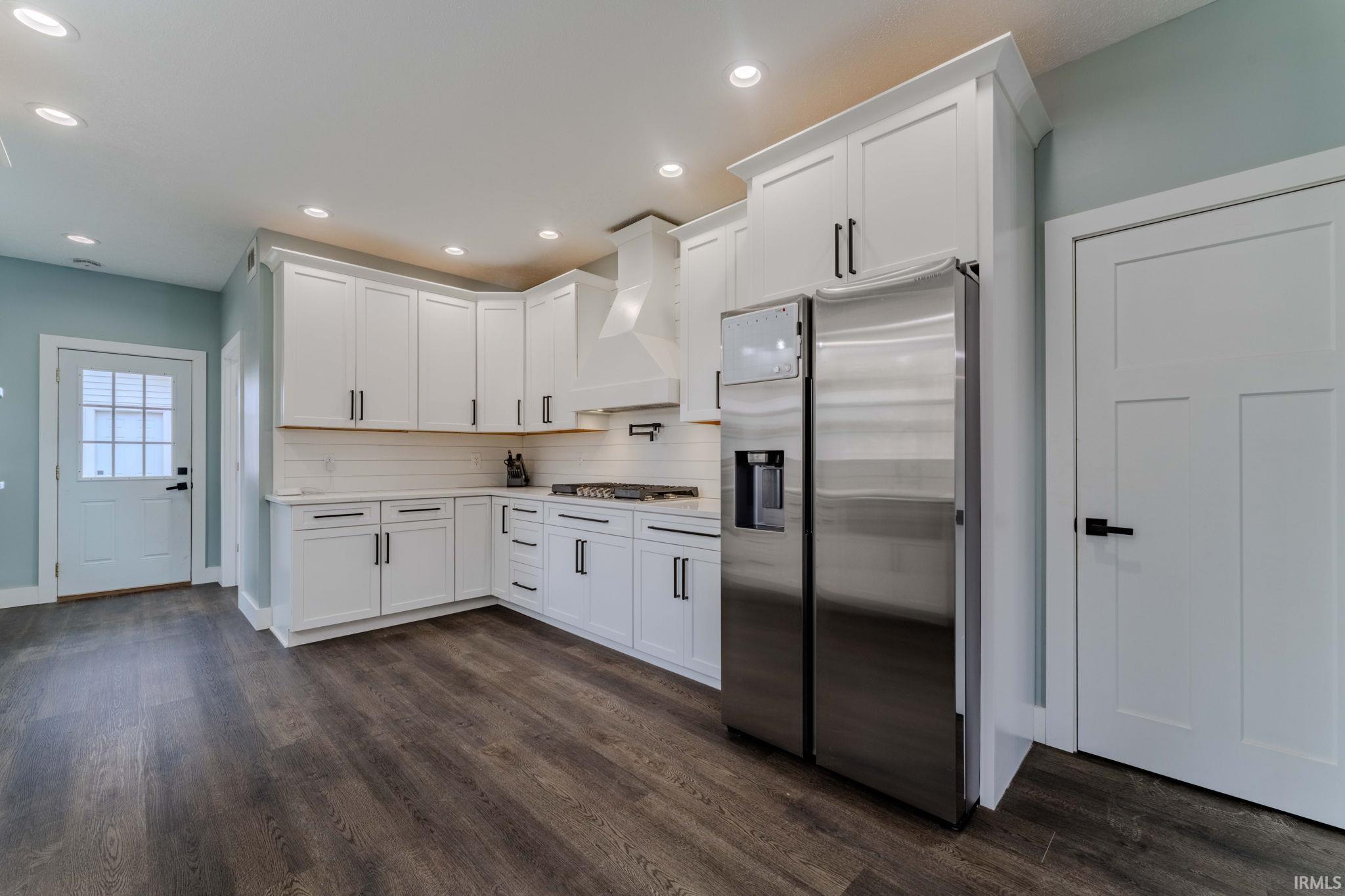 Kitchen featuring stainless steel appliances, white cabinets, premium range hood, dark wood-type flooring, and recessed lighting