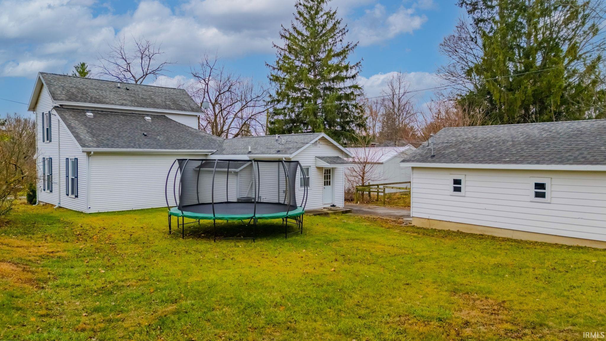 Rear view of house featuring a trampoline, roof with shingles, and a yard