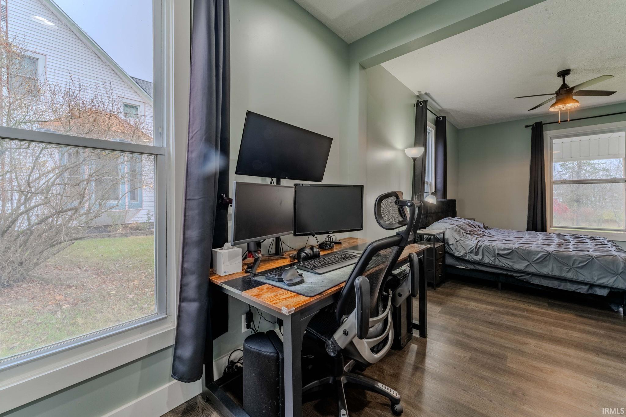 Bedroom with a desk, dark wood-style flooring, and a ceiling fan