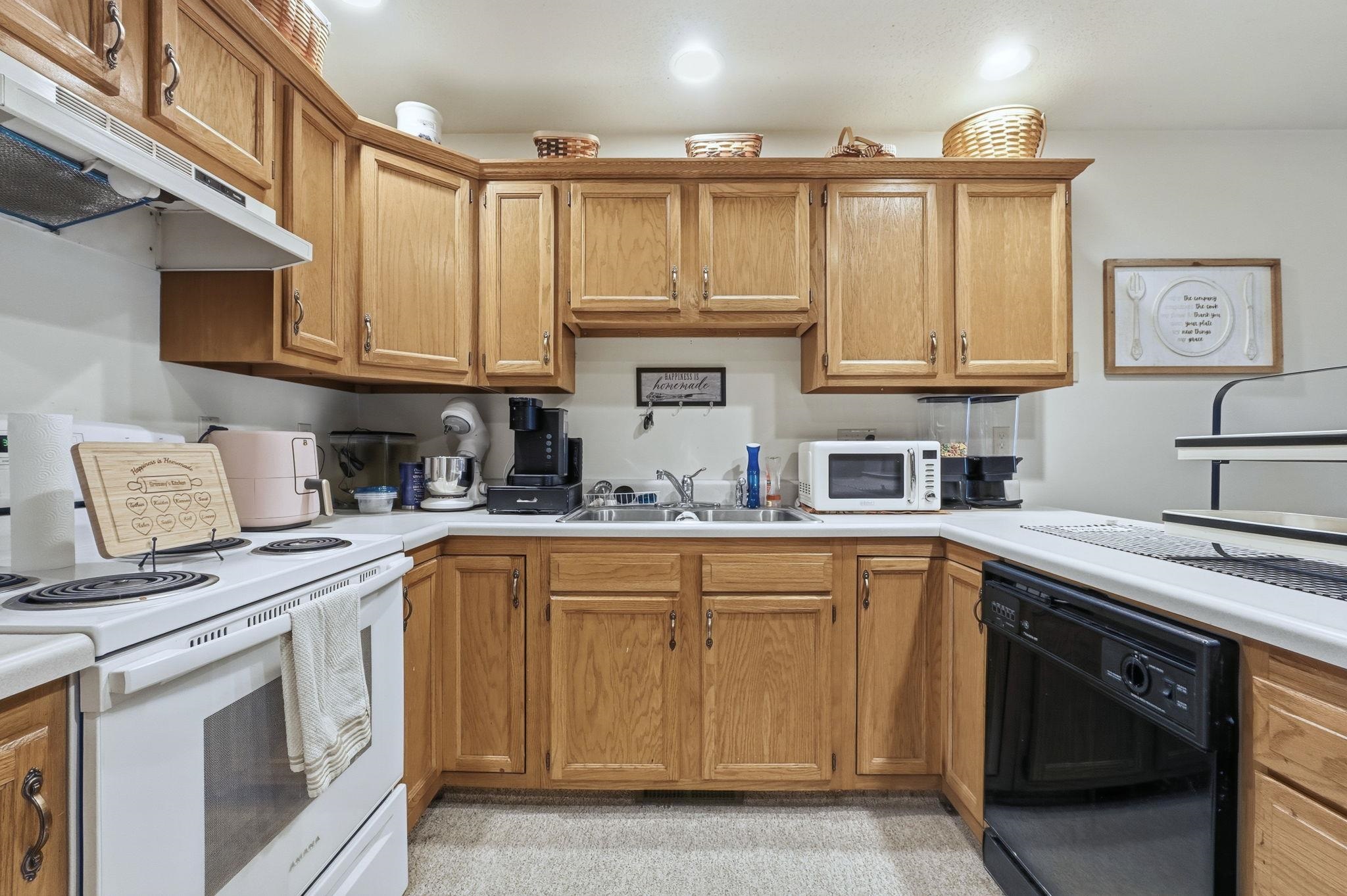 Kitchen featuring white appliances, under cabinet range hood, light countertops, and brown cabinetry