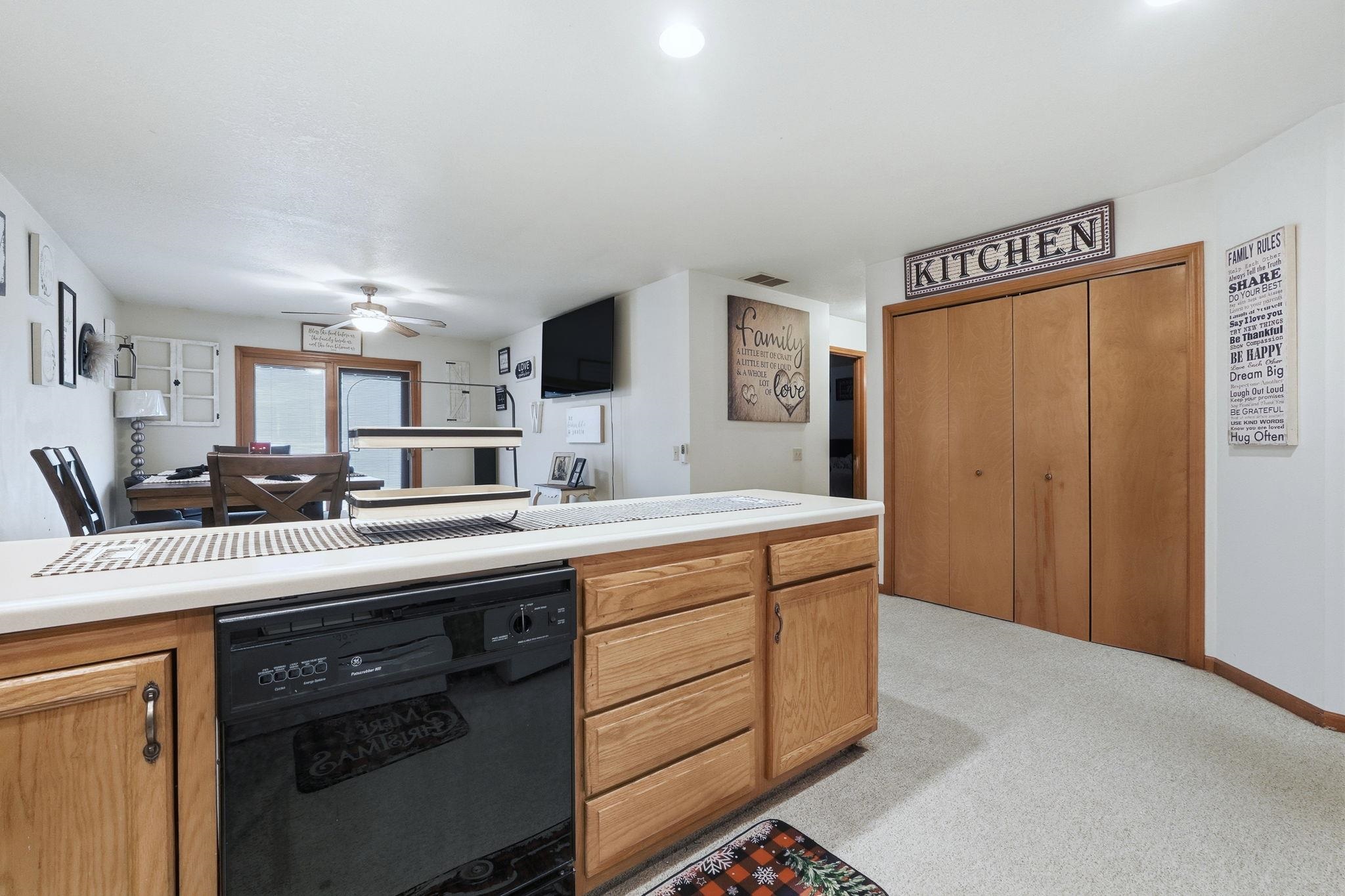Kitchen with dishwasher, light countertops, light colored carpet, and ceiling fan