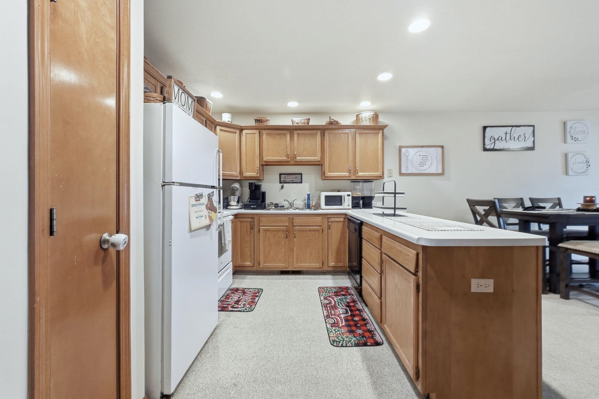 Kitchen featuring white appliances, light countertops, a peninsula, brown cabinets, and recessed lighting