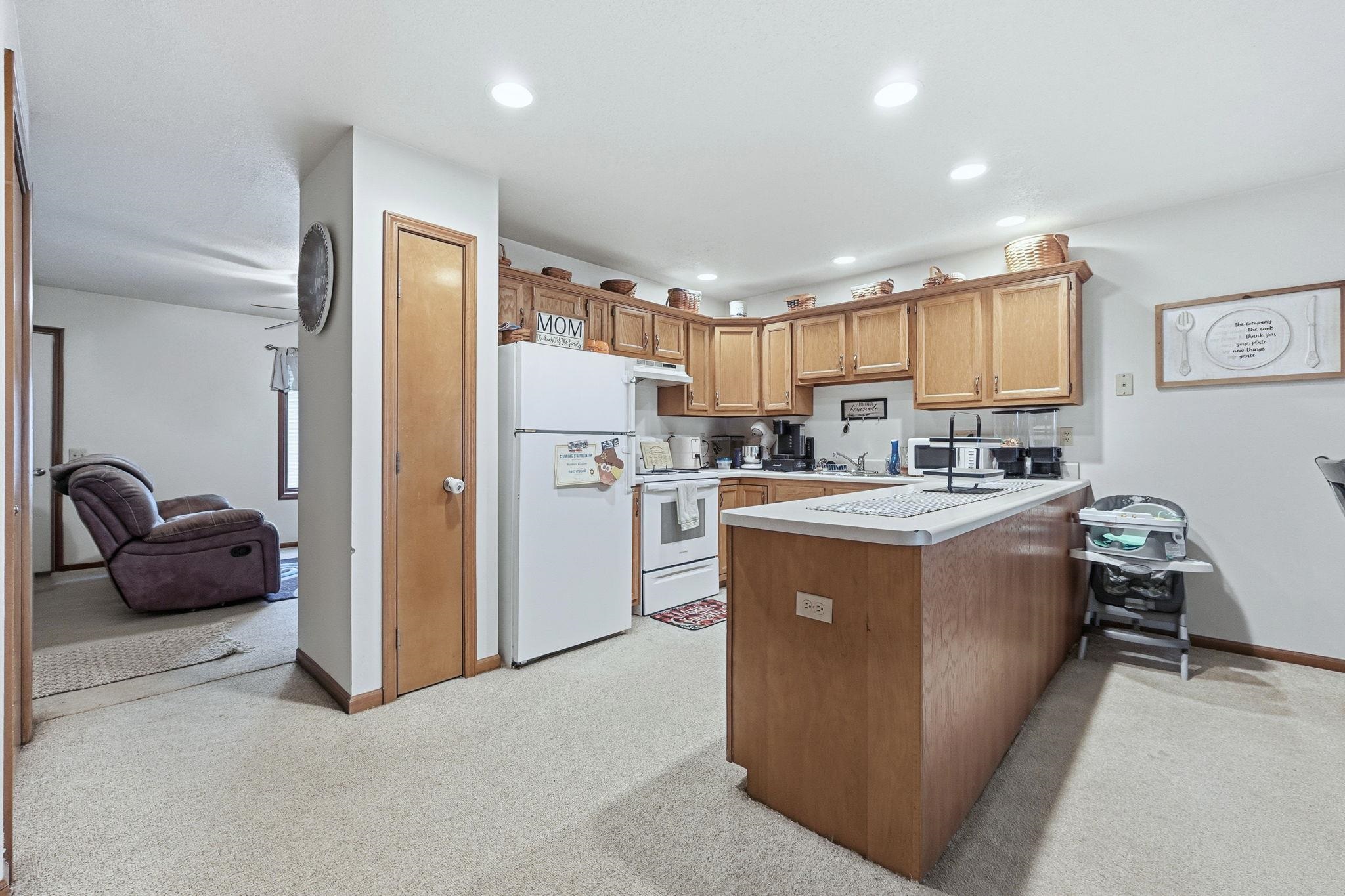 Kitchen with a peninsula, light countertops, white appliances, light carpet, and recessed lighting
