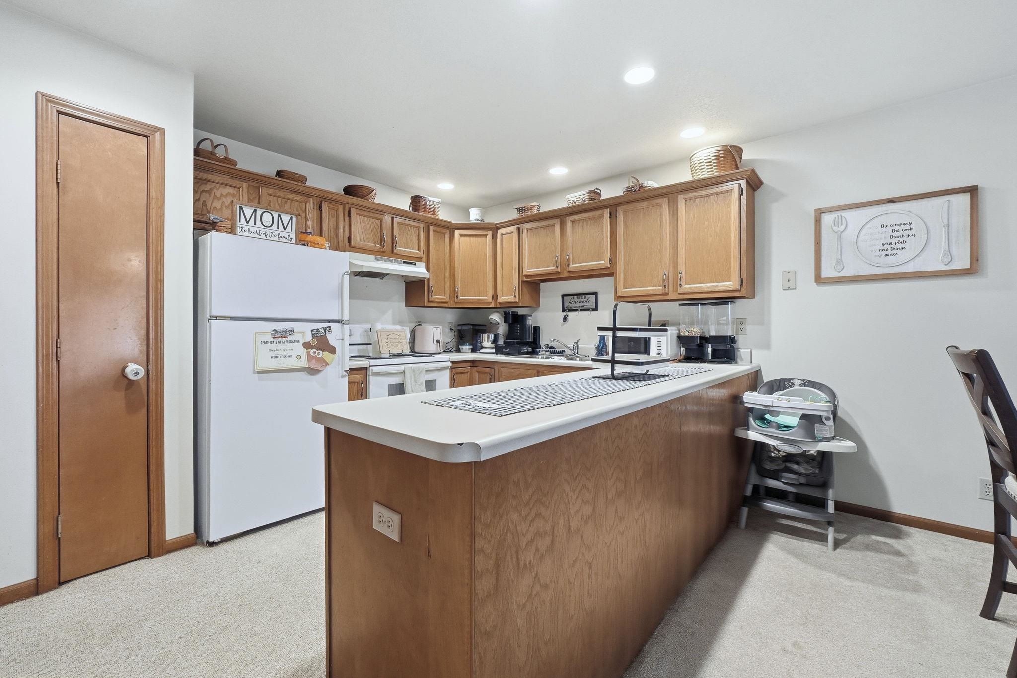 Kitchen with a peninsula, white appliances, light countertops, brown cabinets, and light carpet