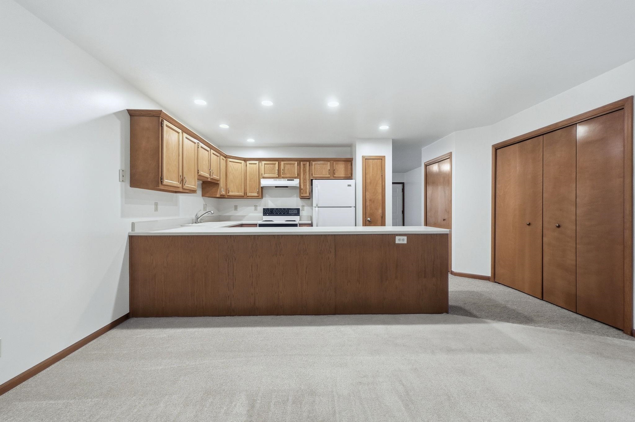 Kitchen with a peninsula, light countertops, recessed lighting, freestanding refrigerator, and light colored carpet