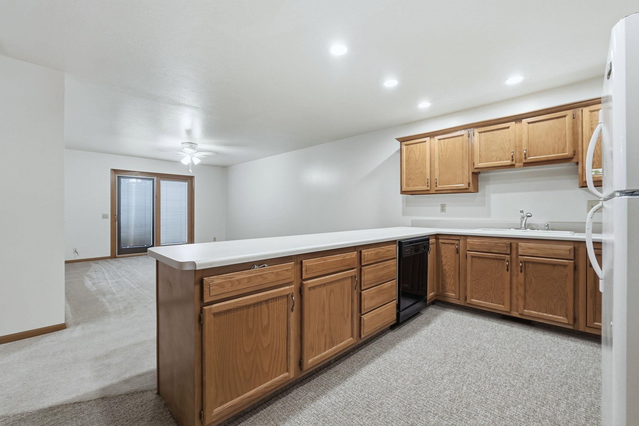 Kitchen featuring light carpet, a peninsula, freestanding refrigerator, light countertops, and recessed lighting