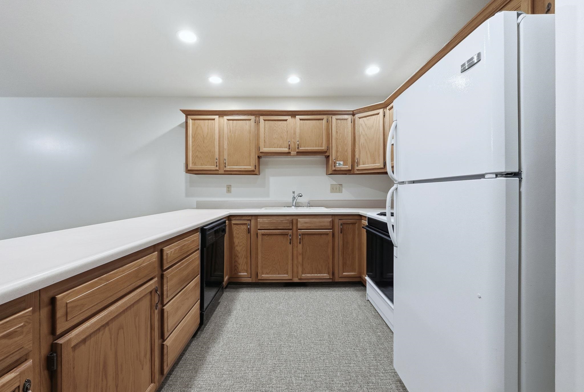 Kitchen featuring freestanding refrigerator, recessed lighting, light countertops, stove, and brown cabinetry