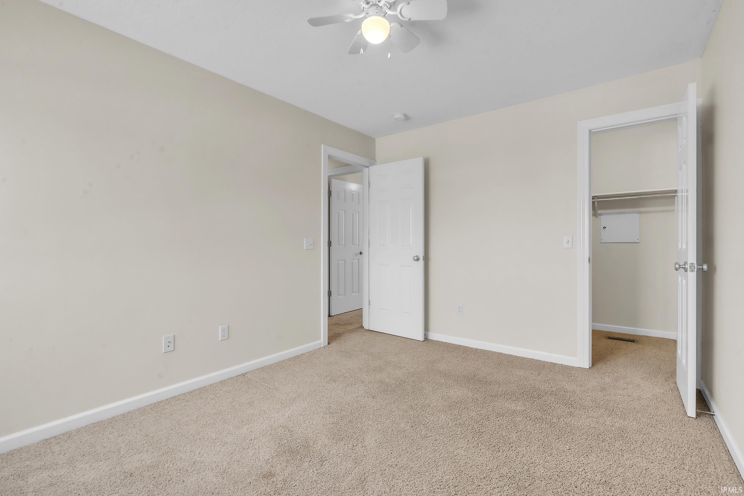 Unfurnished bedroom with a spacious closet, light carpet, and a ceiling fan
