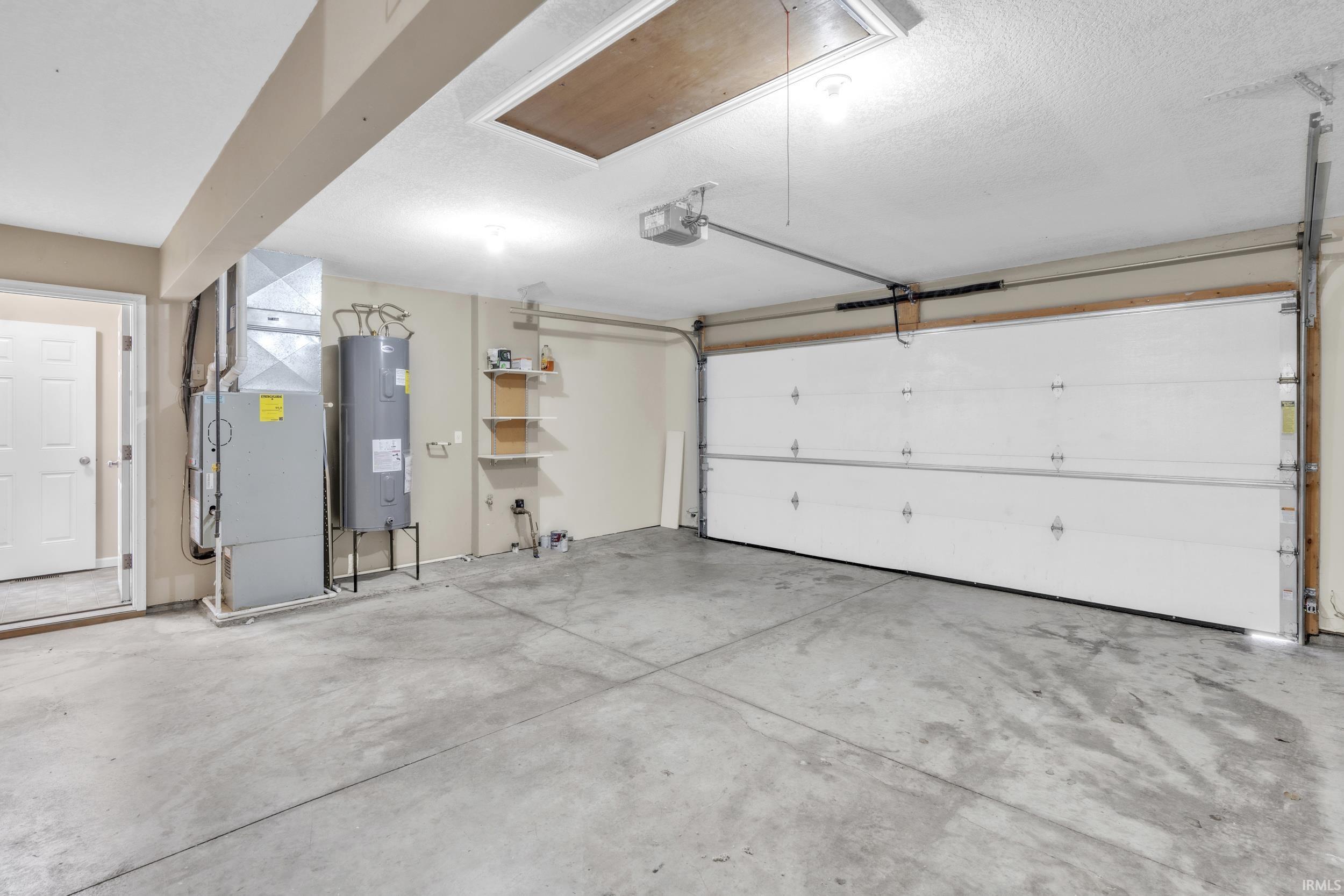 Garage featuring heating unit, electric water heater, and a garage door opener