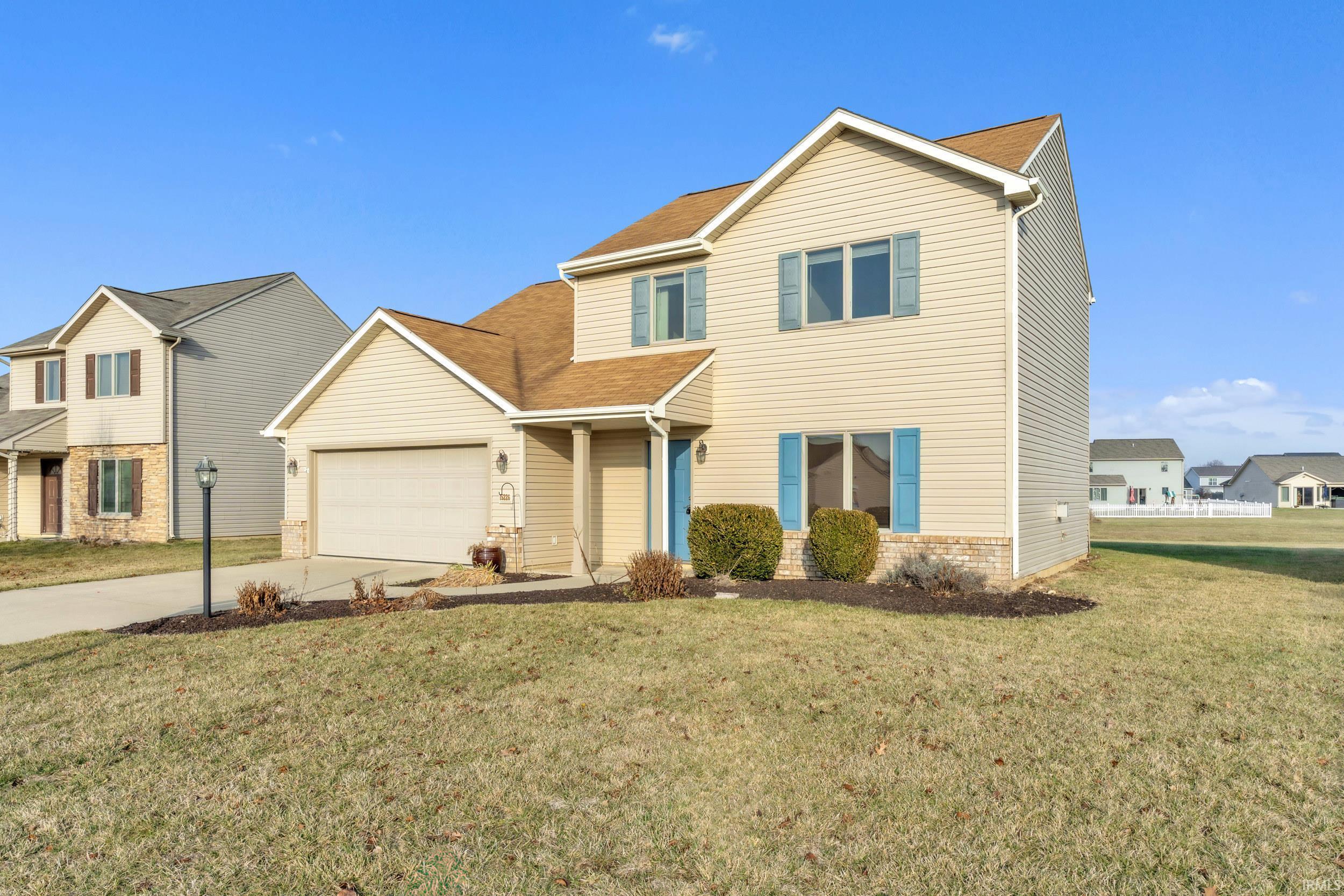 Traditional-style house featuring a front yard, driveway, brick siding, roof with shingles, and an attached garage
