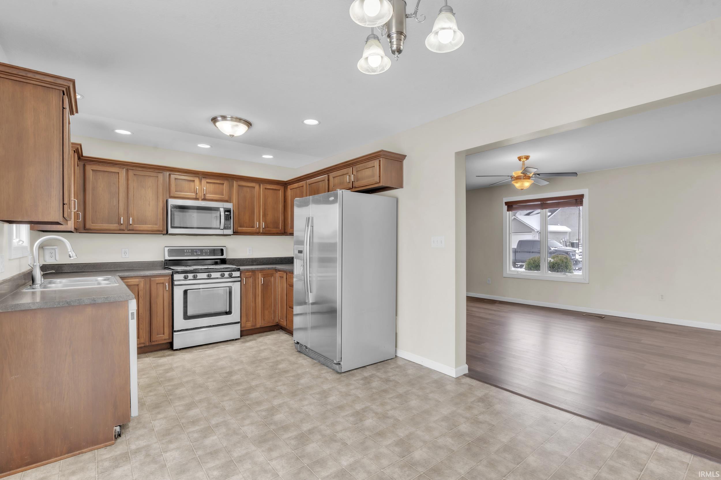 Kitchen featuring appliances with stainless steel finishes, brown cabinetry, dark countertops, hanging light fixtures, and recessed lighting