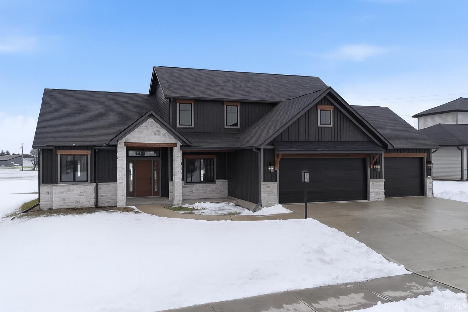 View of front facade featuring stone siding, roof with shingles, concrete driveway, and board and batten siding