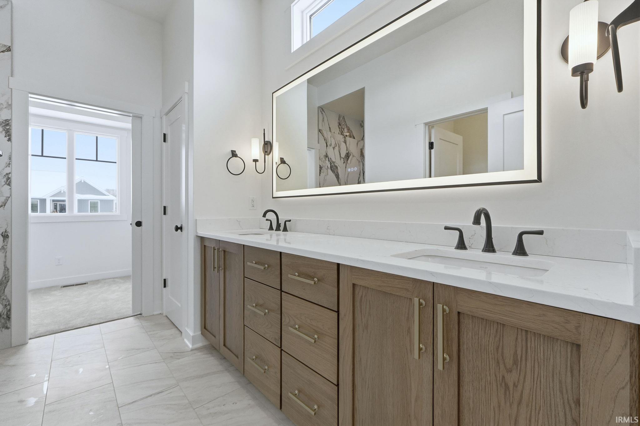 Bathroom with healthy amount of natural light, light marble finish flooring, double vanity, and a marble finish shower