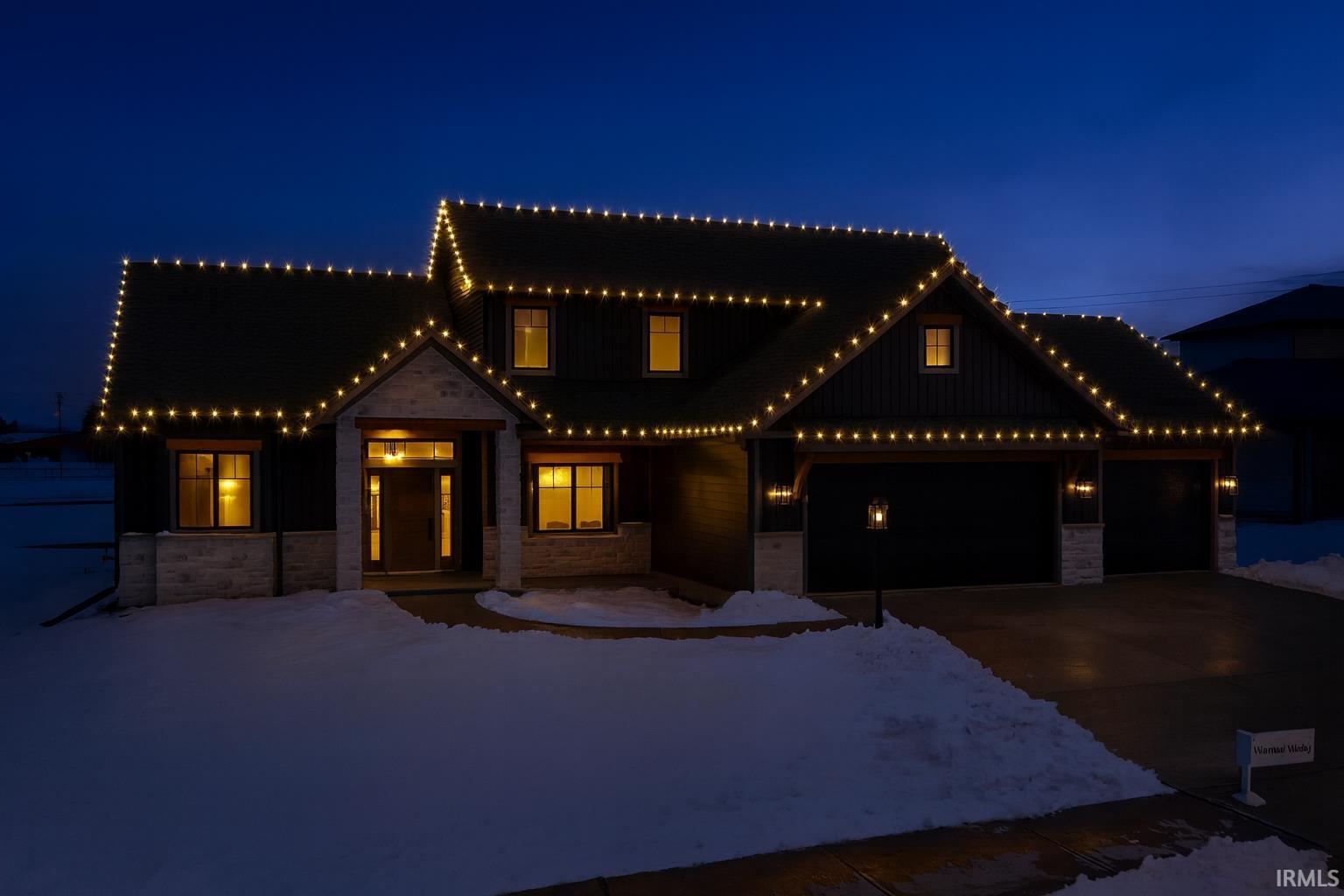 View of front of house with stone siding, an attached garage, concrete driveway, and board and batten siding
