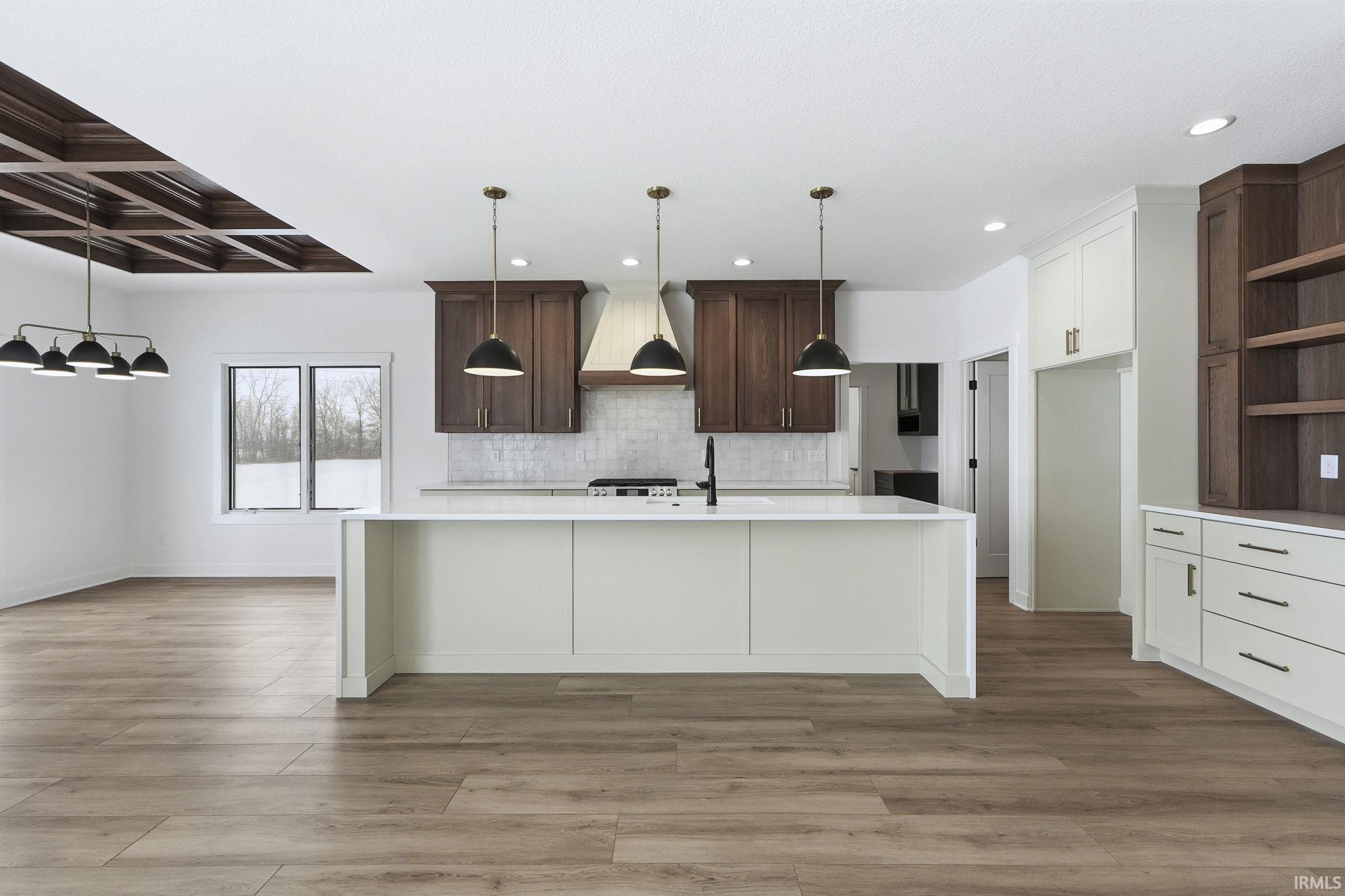 Kitchen with pendant lighting, an island with sink, custom range hood, open shelves, and light wood-type flooring