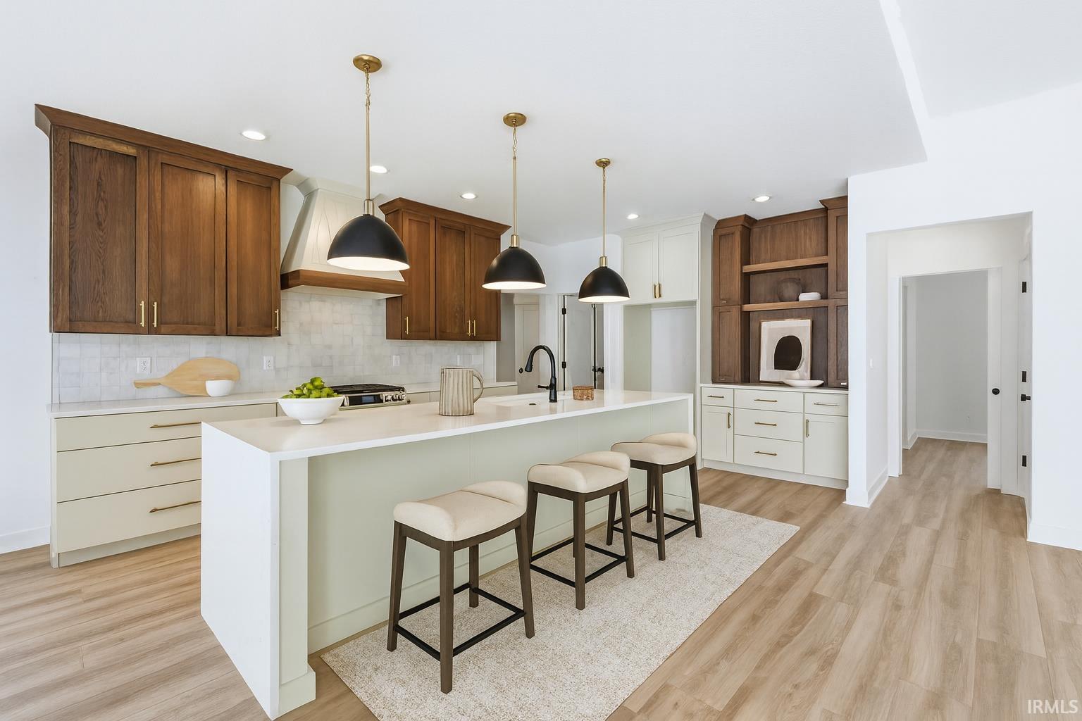 Kitchen with a kitchen bar, a center island with sink, custom exhaust hood, hanging light fixtures, and light wood-style floors
