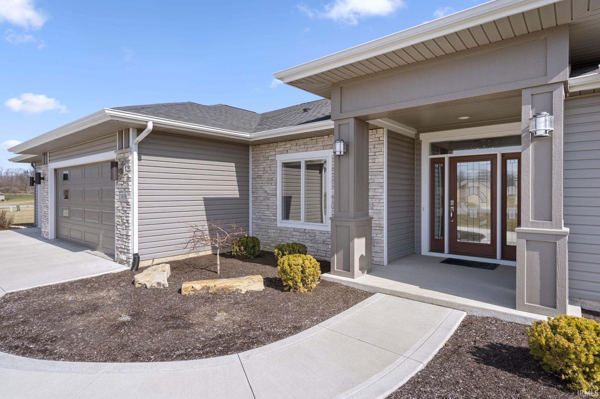 View of exterior entry with an attached garage, stone siding, covered porch, concrete driveway, and a shingled roof