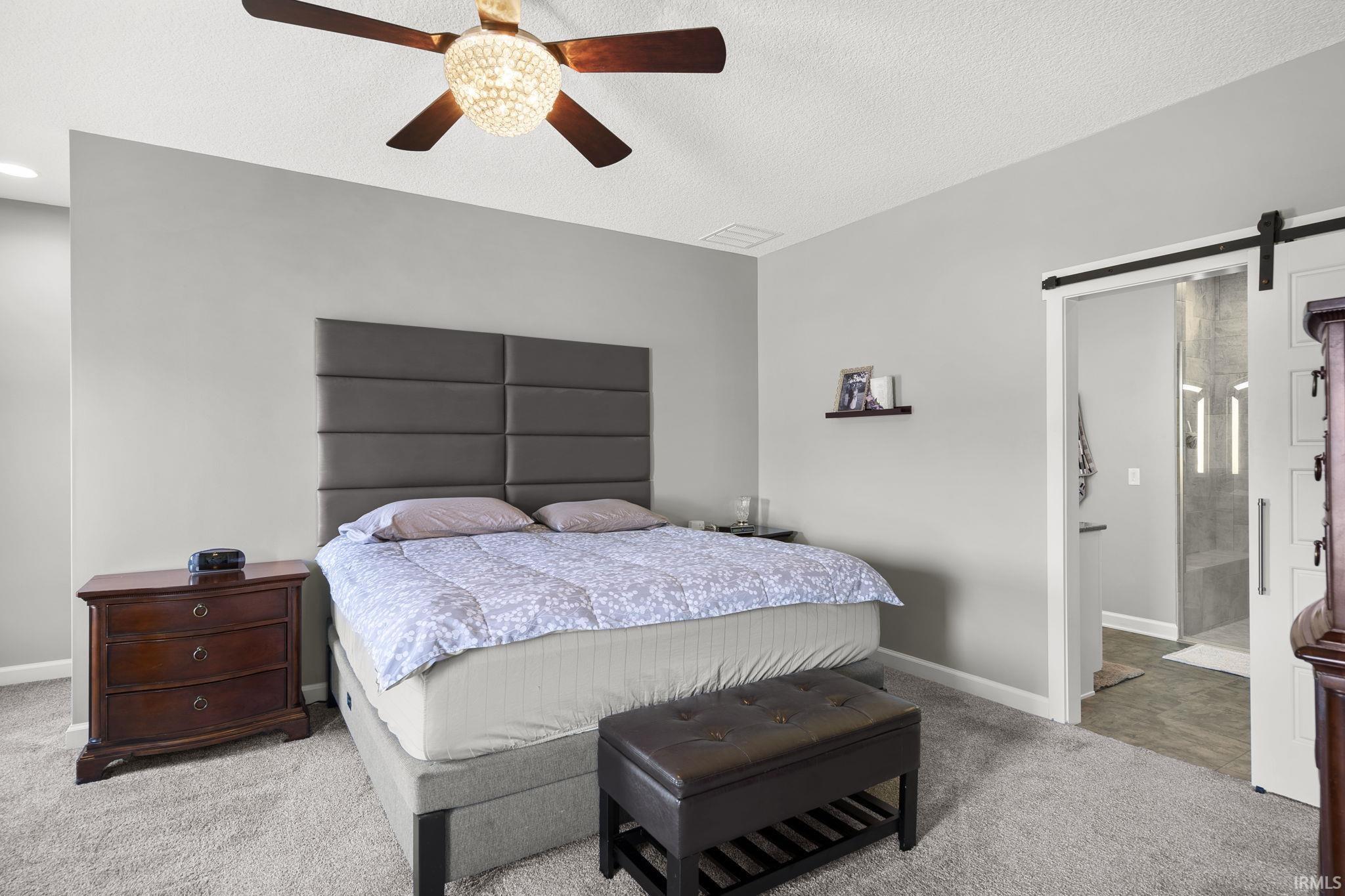 Carpeted bedroom with a barn door, ceiling fan, and a textured ceiling