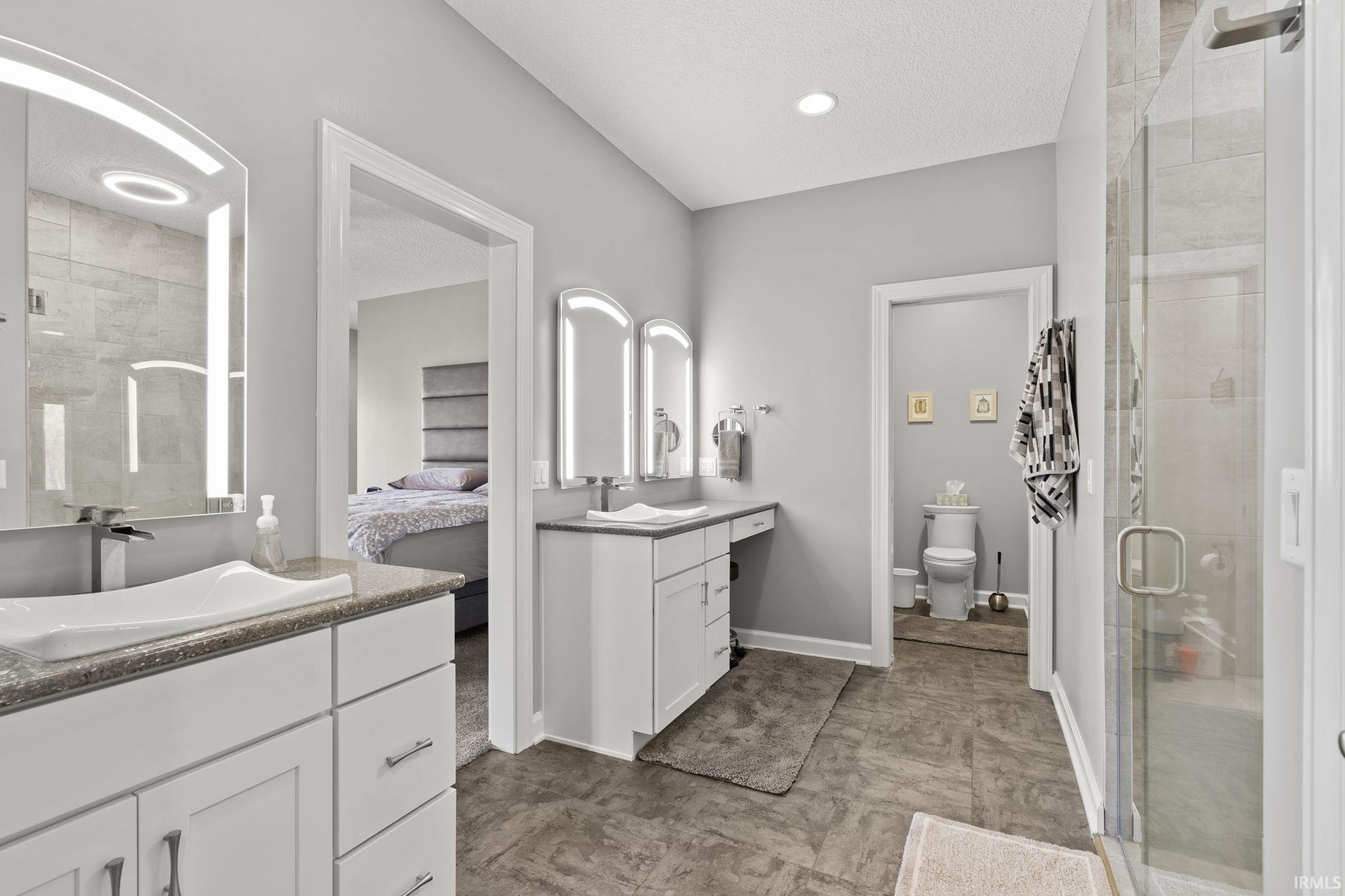 Full bathroom featuring a stall shower, two vanities, ensuite bath, and a textured ceiling