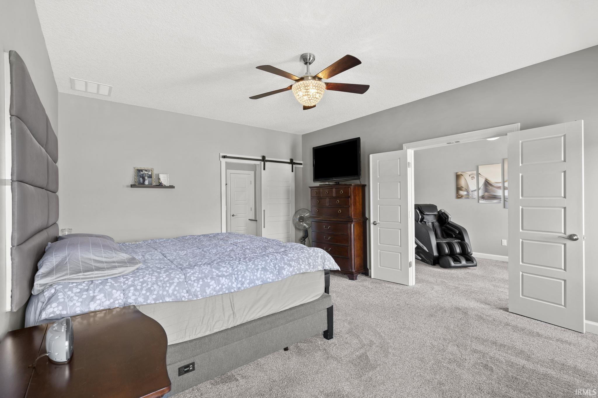 Bedroom with carpet flooring, ceiling fan, and a barn door