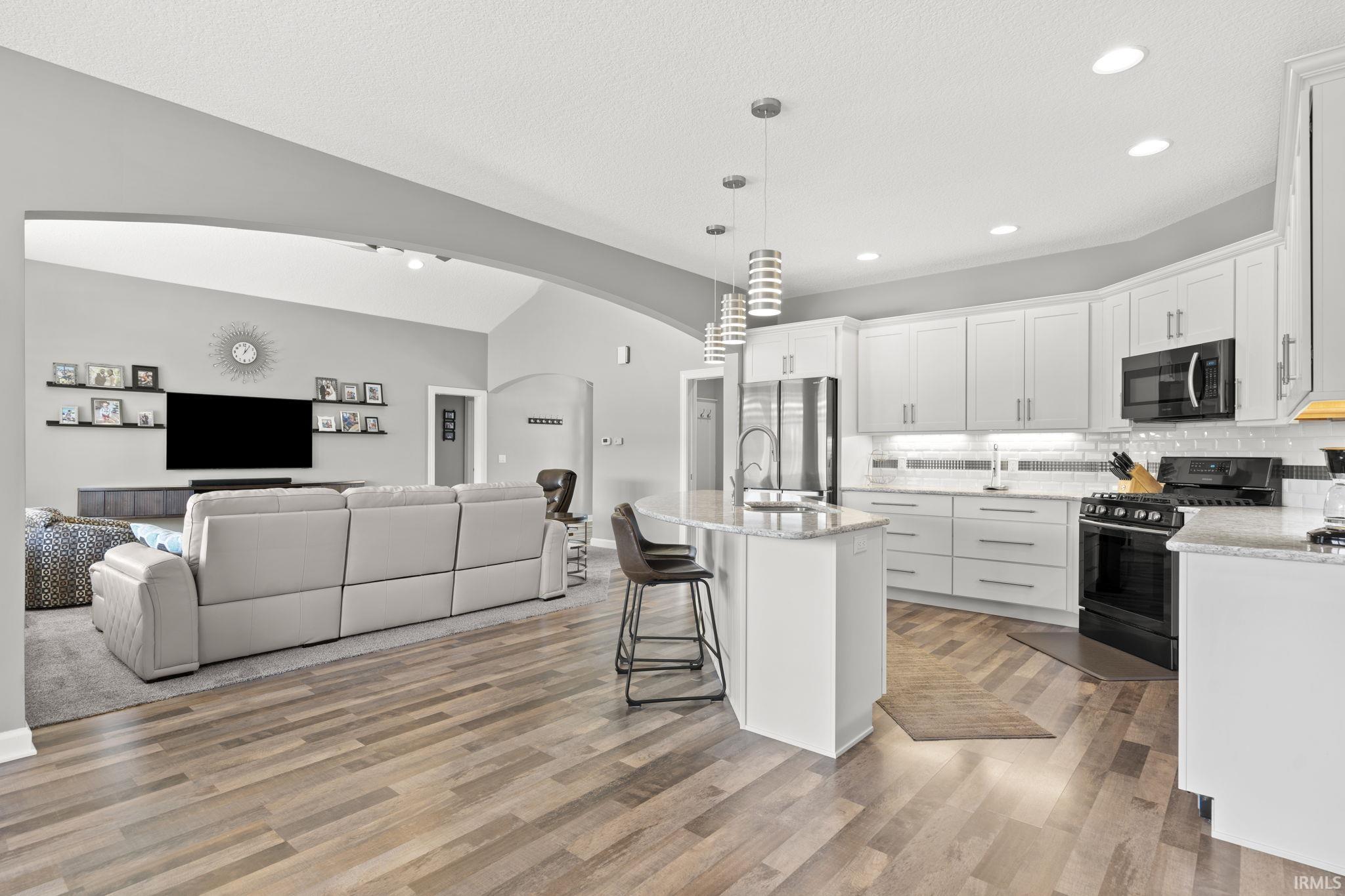 Kitchen with white cabinets, black range with gas cooktop, a breakfast bar, hanging light fixtures, and open floor plan