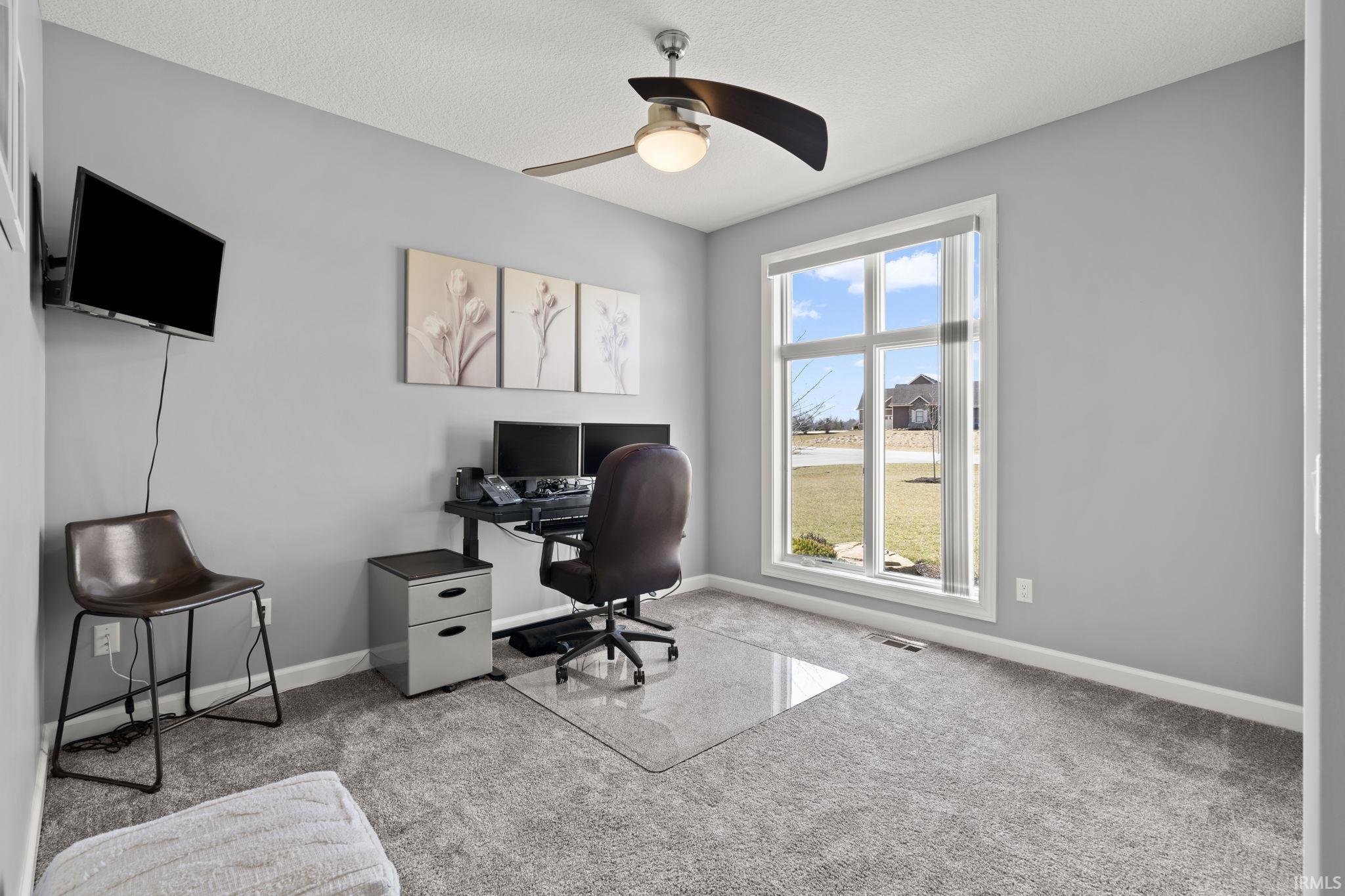Carpeted office space with ceiling fan and a textured ceiling
