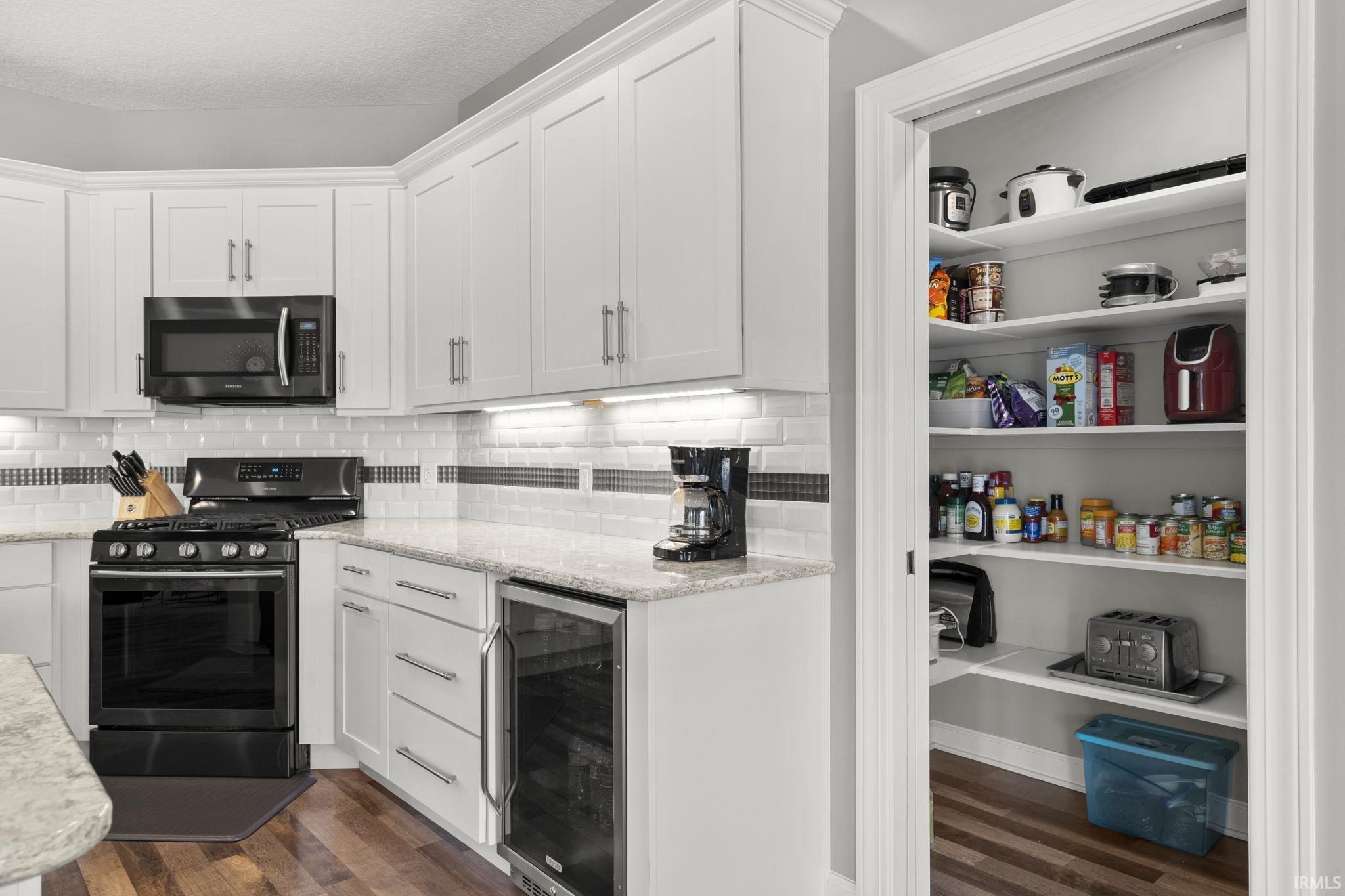 Kitchen with white cabinets, stainless steel appliances, beverage cooler, dark wood finished floors, and a textured ceiling