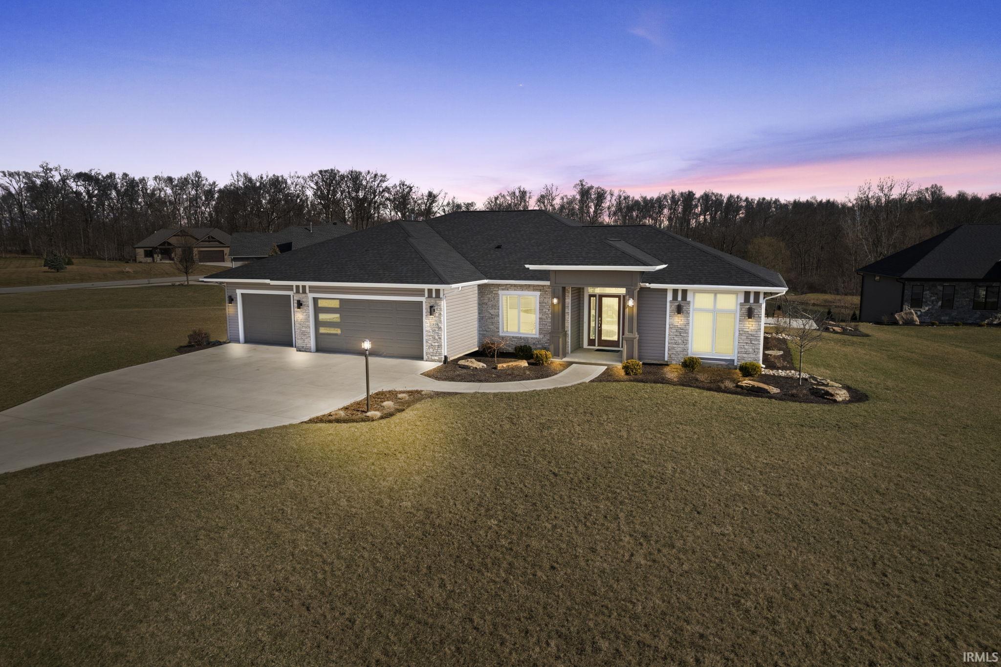 View of front facade with a yard, concrete driveway, and stone siding
