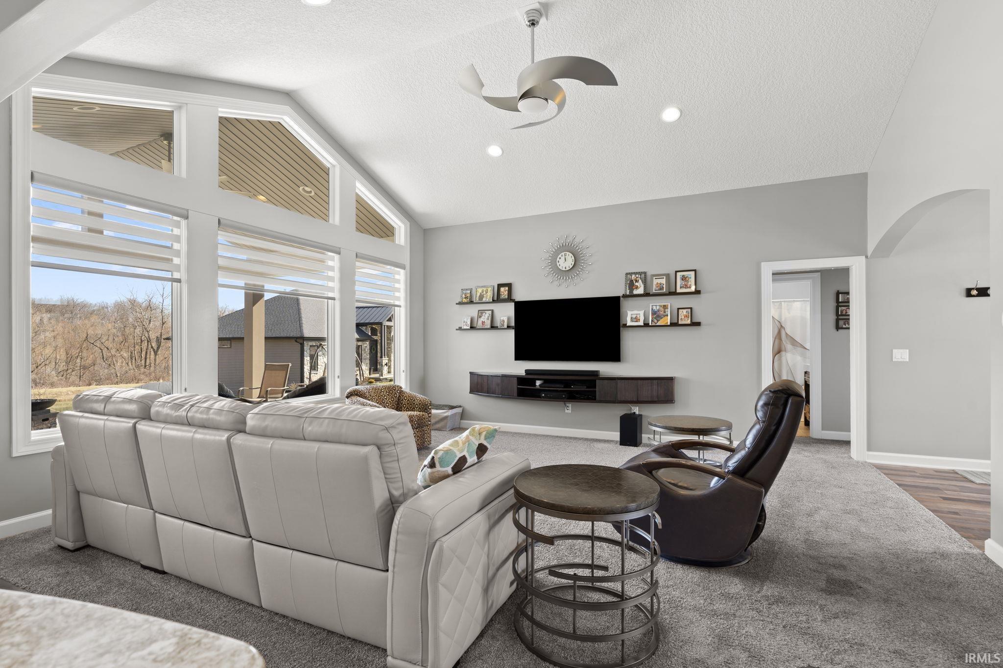 Living area with arched walkways, ceiling fan, a textured ceiling, high vaulted ceiling, and carpet