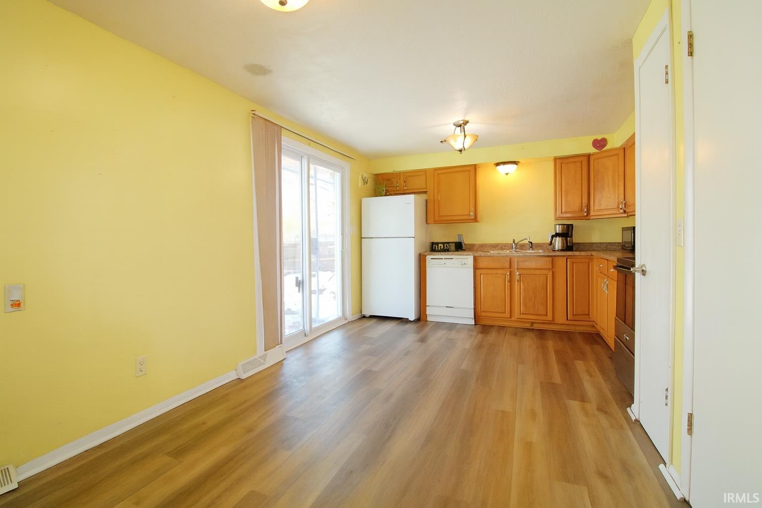 Kitchen with white appliances, brown cabinets, light wood-style flooring, and light countertops