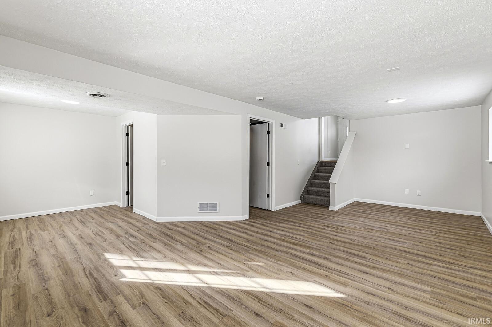 Unfurnished living room featuring a textured ceiling, stairs, and light wood-style flooring