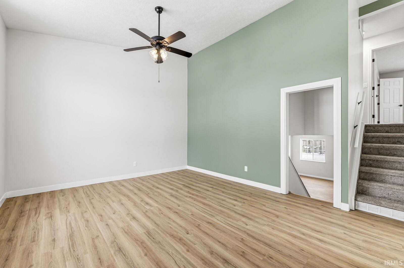 Spare room featuring stairway, light wood-style floors, a ceiling fan, and high vaulted ceiling