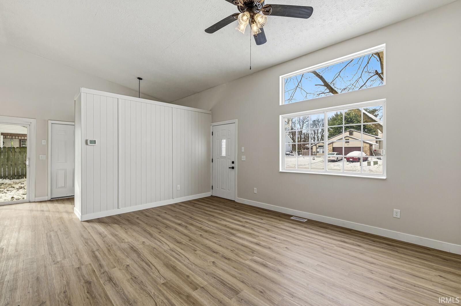 Unfurnished living room with high vaulted ceiling, light wood-style flooring, ceiling fan, and a textured ceiling