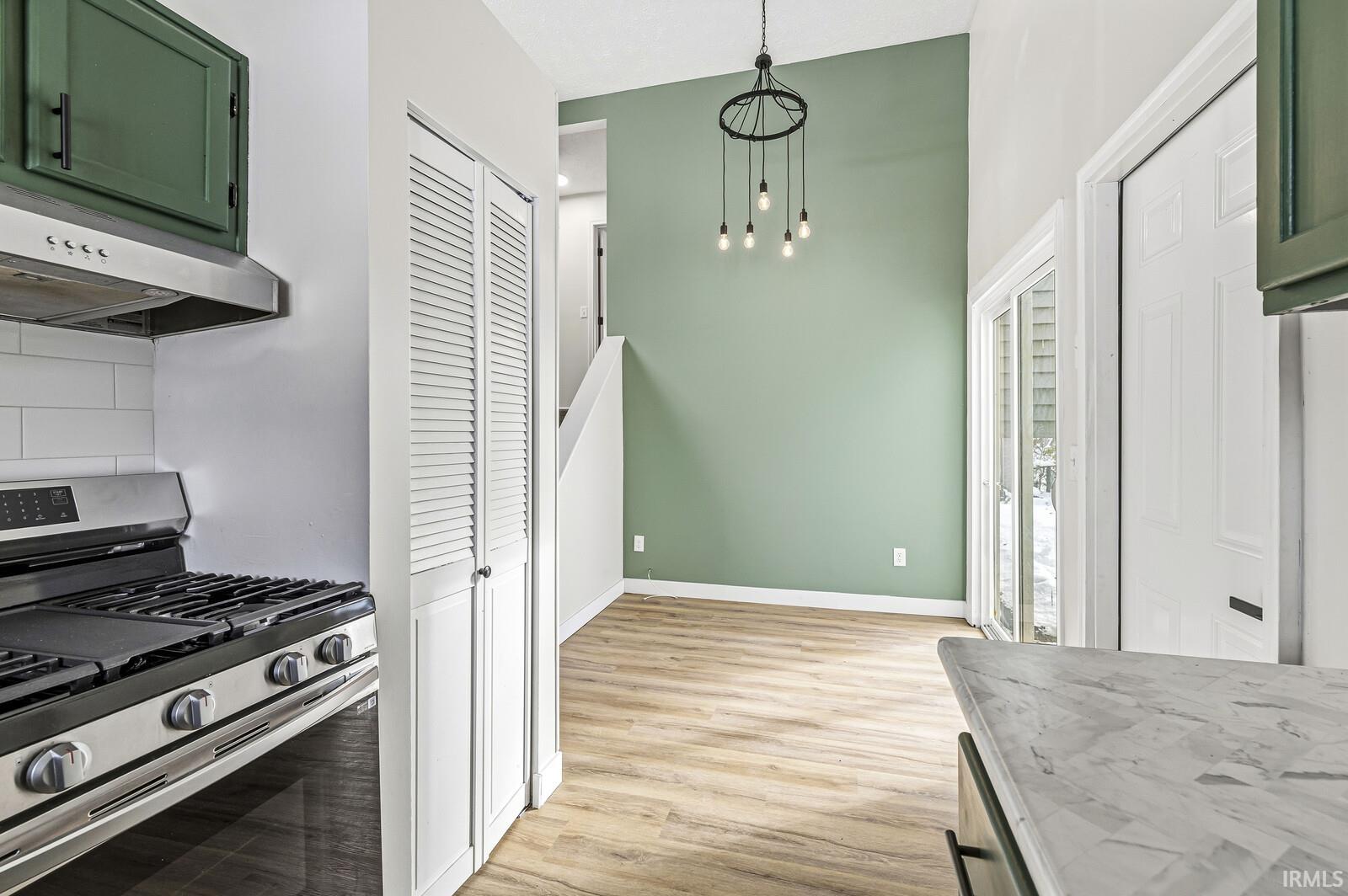 Kitchen with stainless steel range with gas cooktop, green cabinetry, light wood-style flooring, pendant lighting, and decorative backsplash