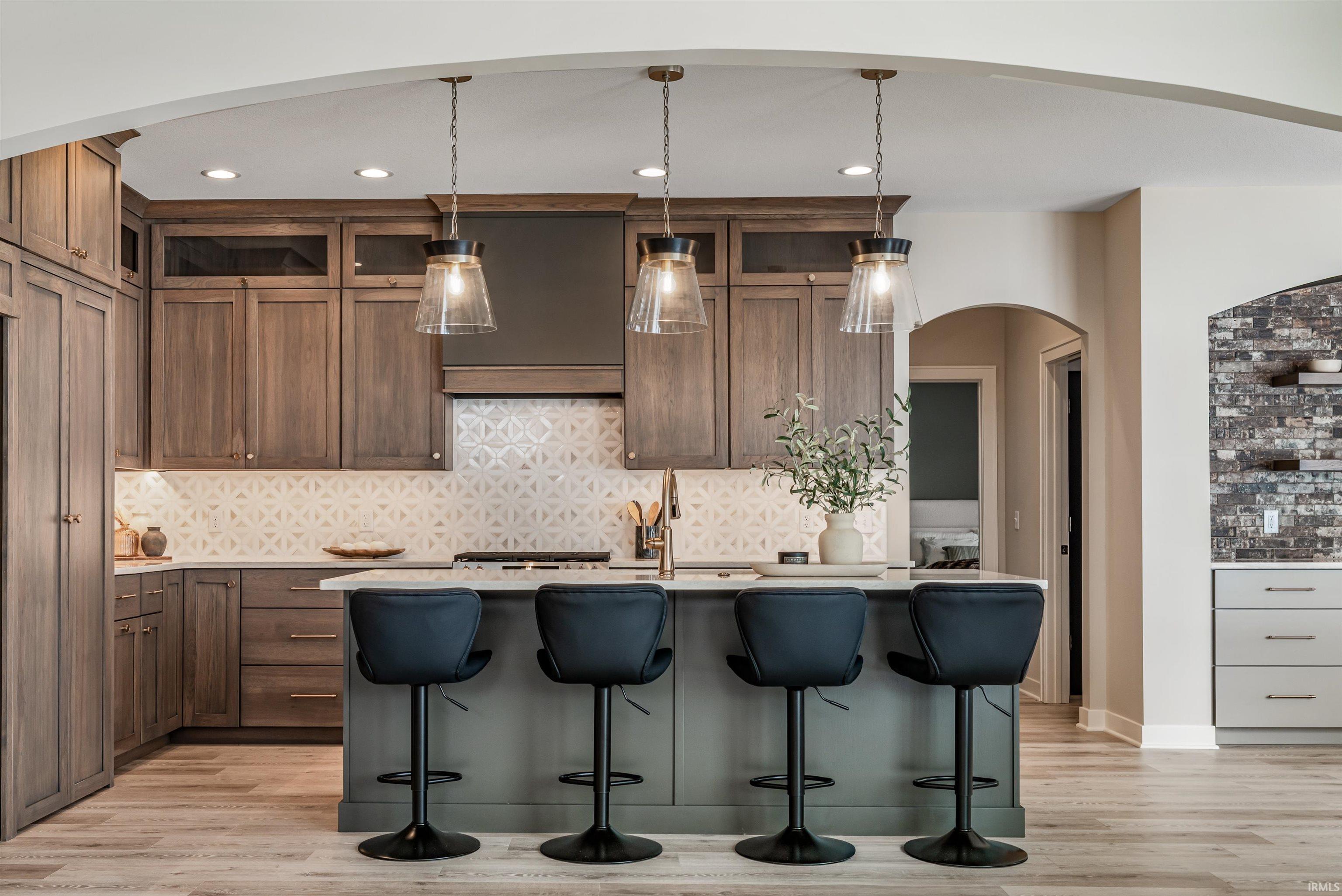 Kitchen featuring backsplash, a center island with sink, pendant lighting, a kitchen breakfast bar, and arched walkways