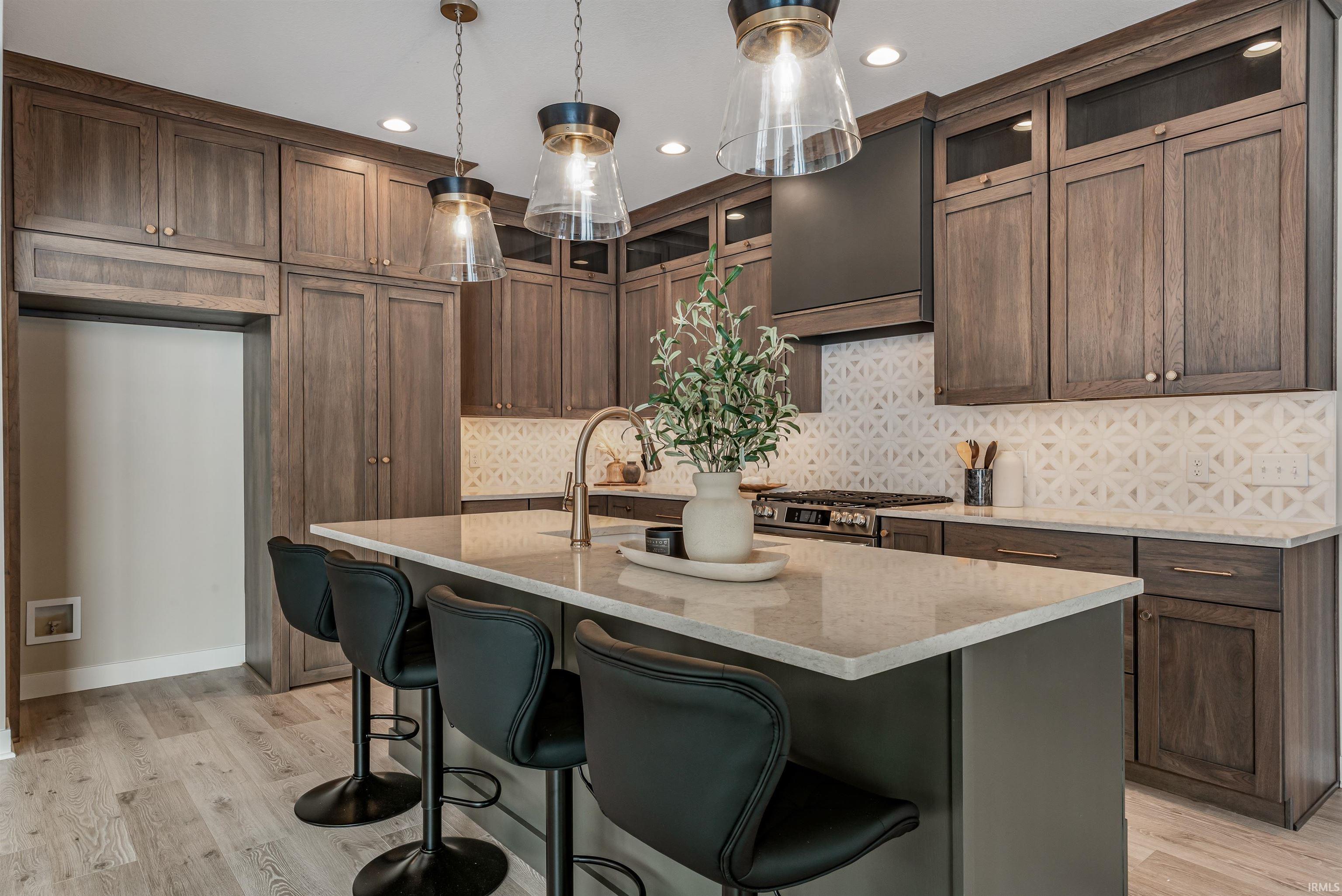 Kitchen with a kitchen bar, light stone counters, a center island with sink, decorative light fixtures, and tasteful backsplash
