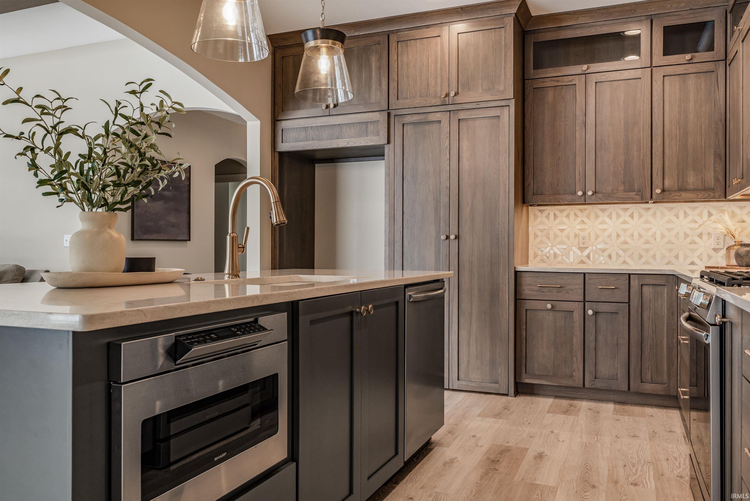 Kitchen featuring hanging light fixtures, stainless steel appliances, backsplash, light wood-style floors, and light stone counters