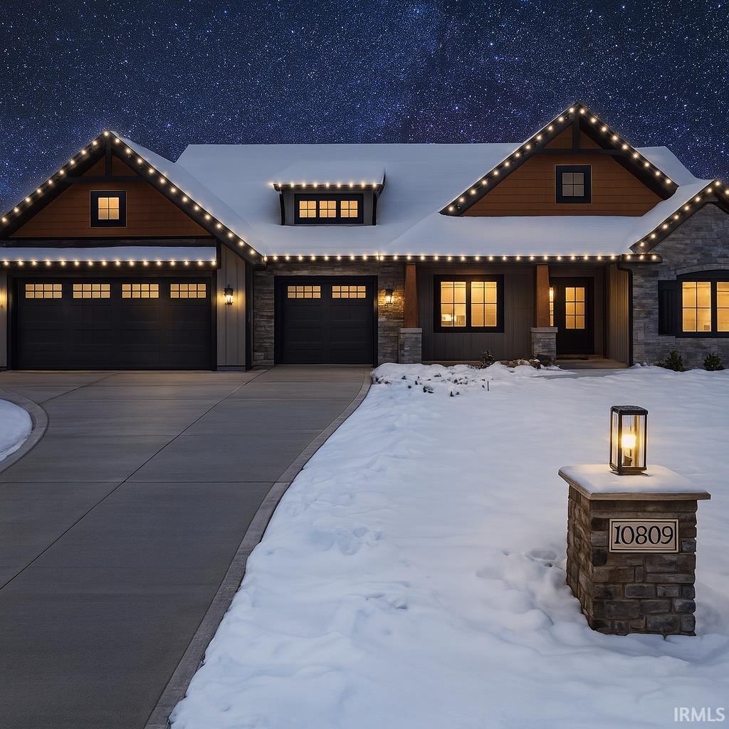 View of front of house with stone siding, a garage, driveway, and board and batten siding
