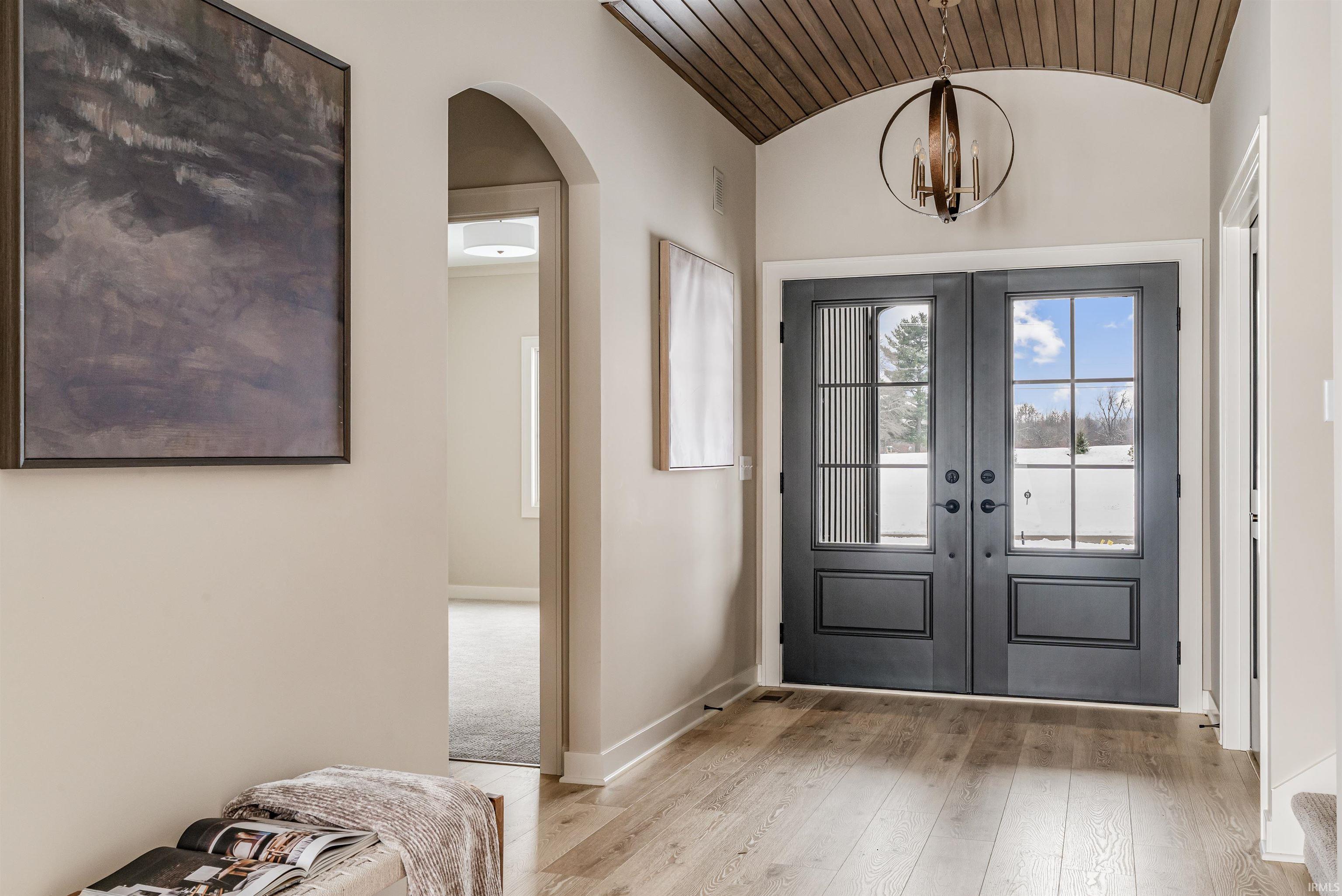 Foyer entrance with arched walkways, lofted ceiling, light wood-type flooring, french doors, and a chandelier