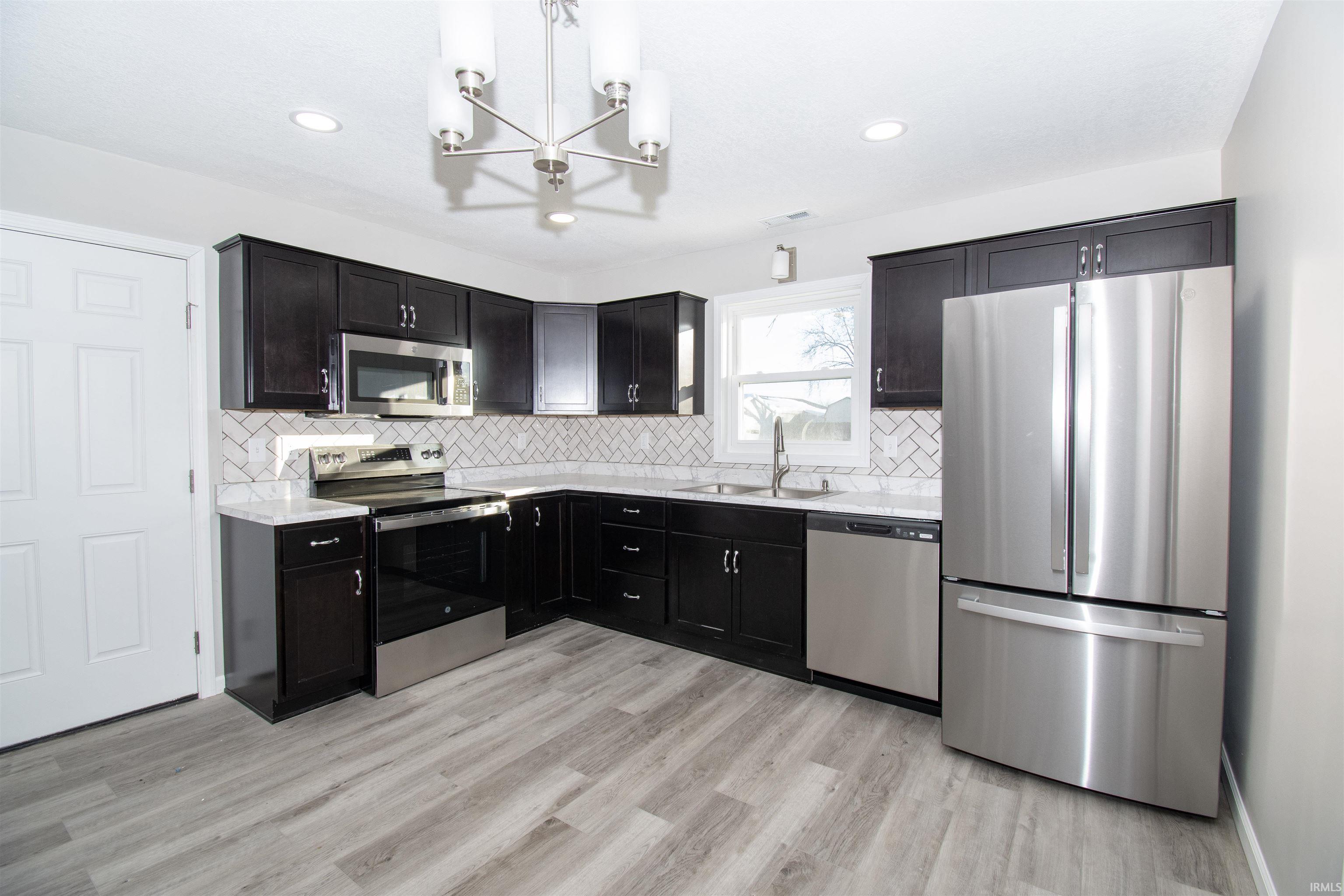 Kitchen with appliances with stainless steel finishes, decorative backsplash, dark cabinets, a chandelier, and recessed lighting