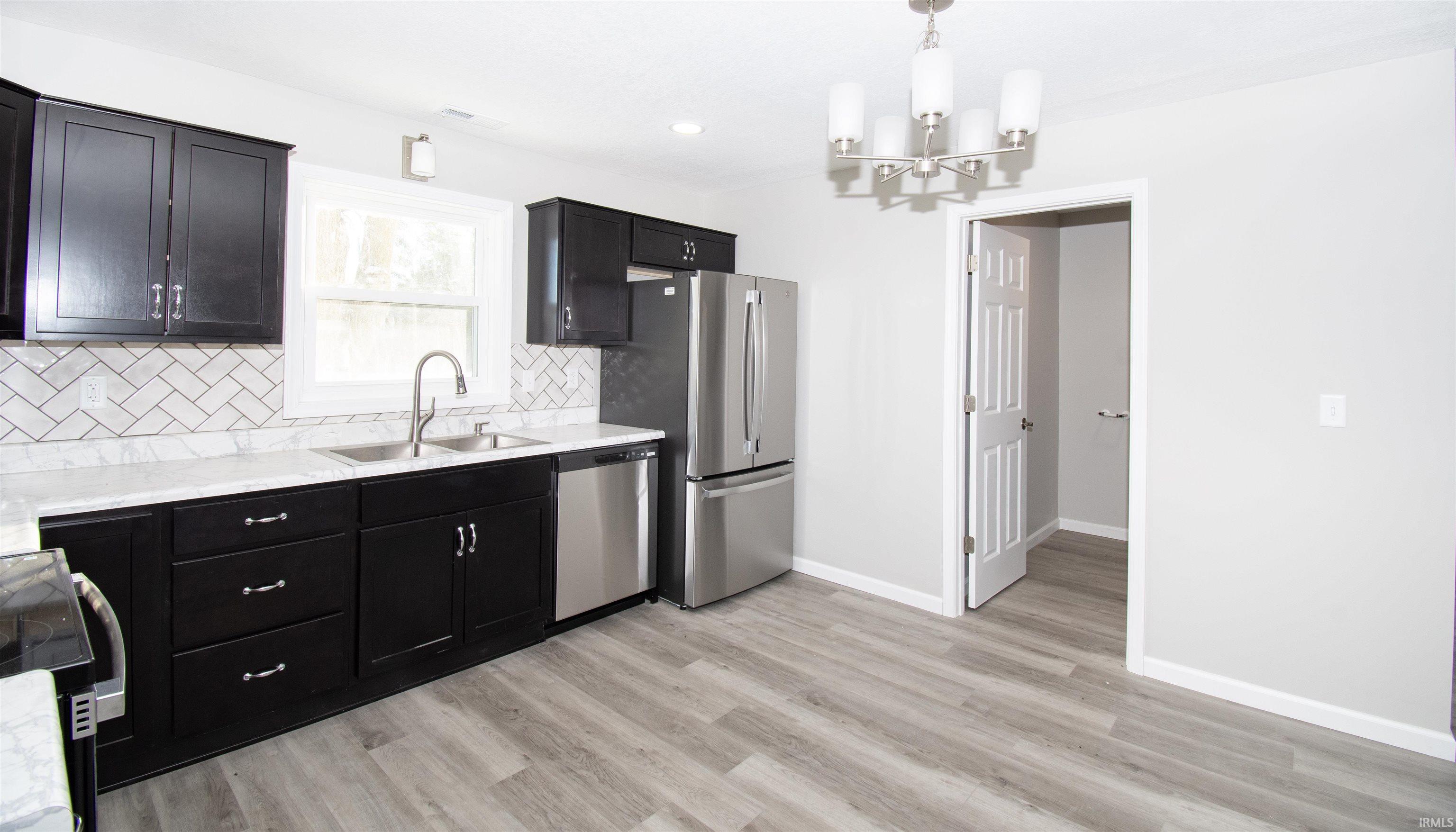 Kitchen featuring stainless steel appliances, backsplash, dark cabinetry, pendant lighting, and light wood-type flooring