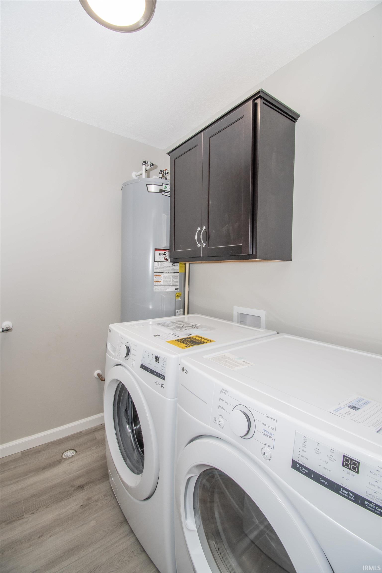 Washroom featuring cabinet space, light wood finished floors, washer and dryer, and electric water heater